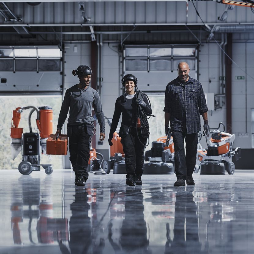 Three people are walking in a warehouse carrying tools
