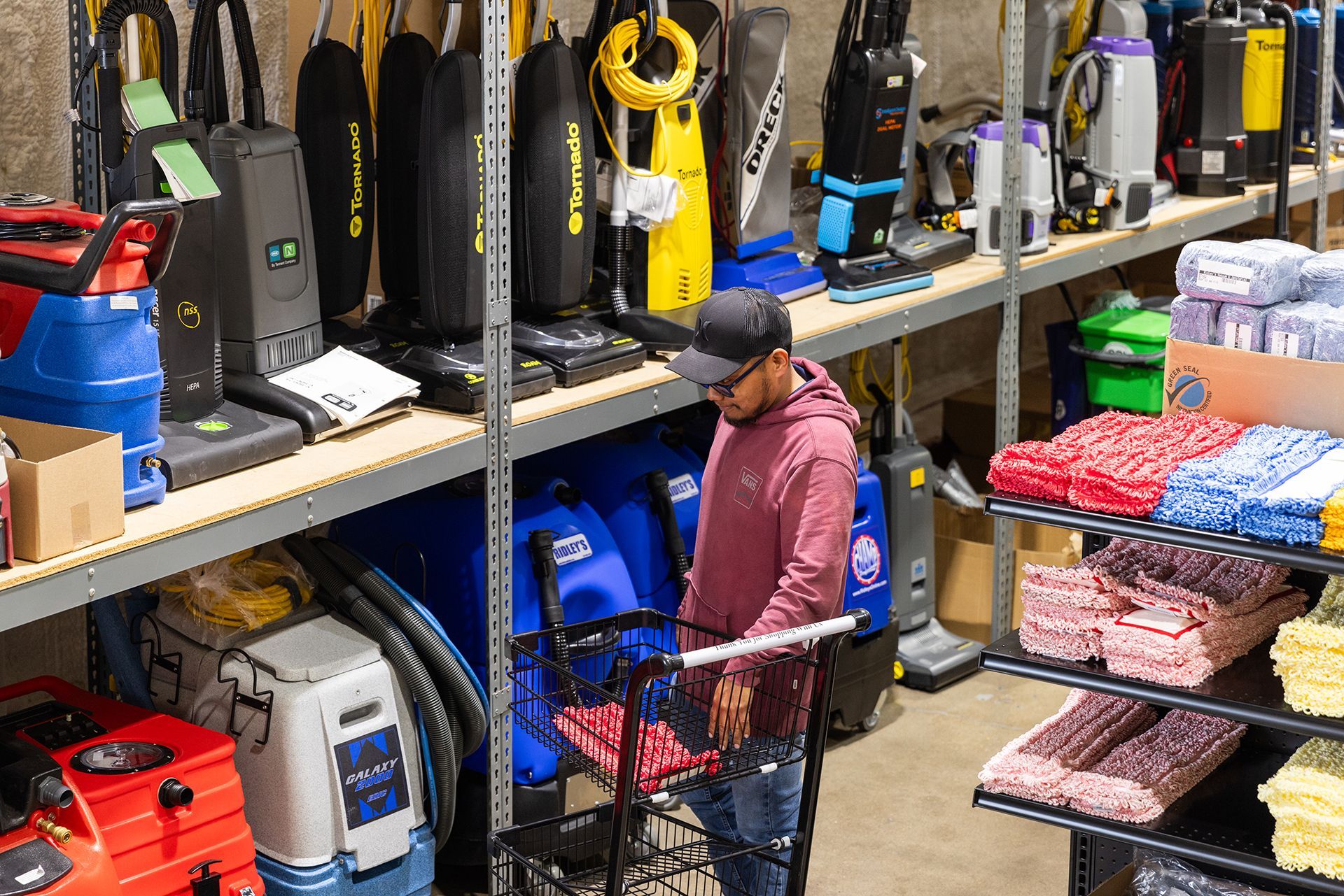A man is standing in a warehouse looking at vacuum cleaners.