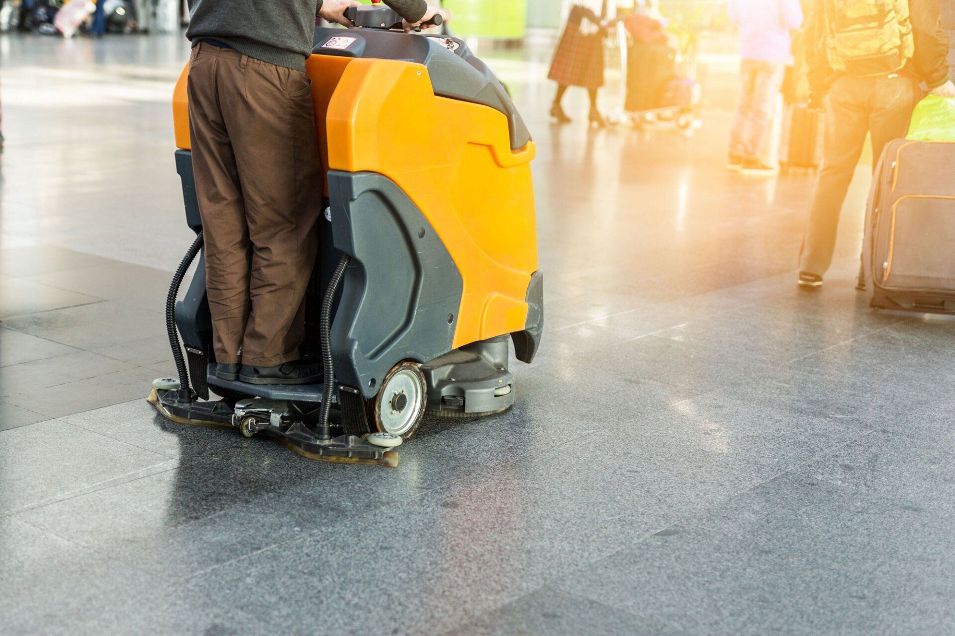 A man is cleaning the floor of an airport with a machine.