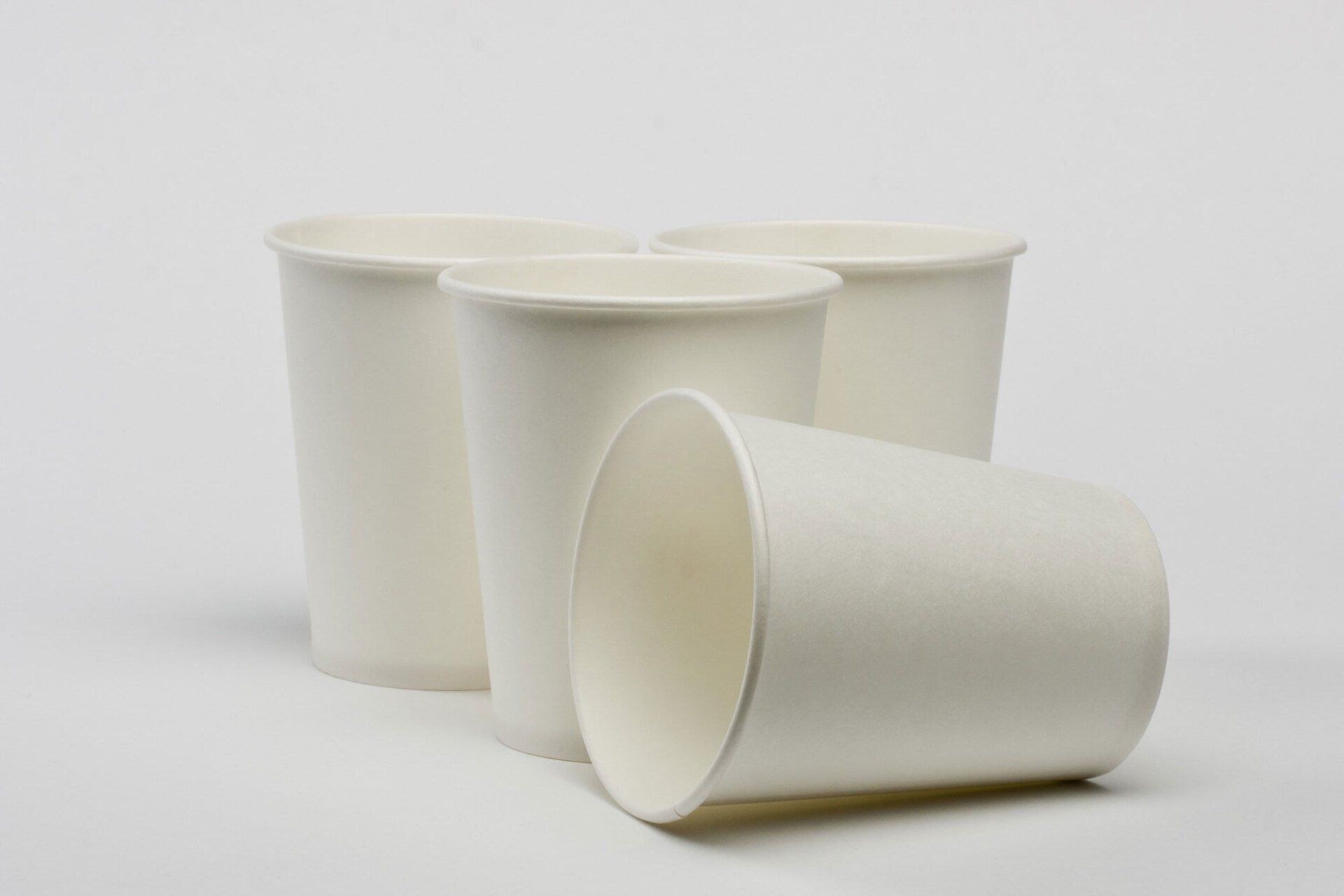 Three white paper cups are stacked on top of each other on a white surface.