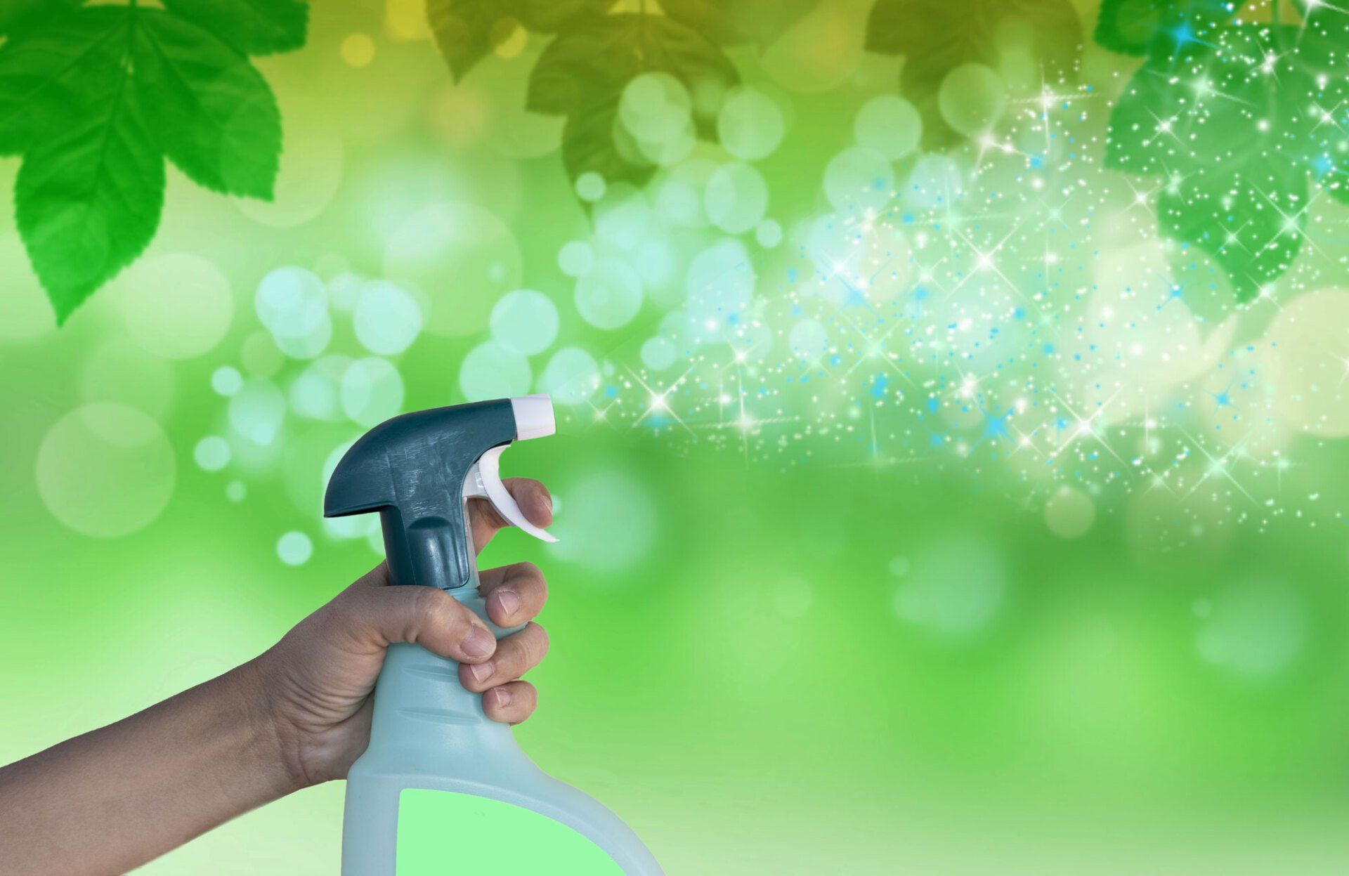 A hand is holding a spray bottle in front of a green background.