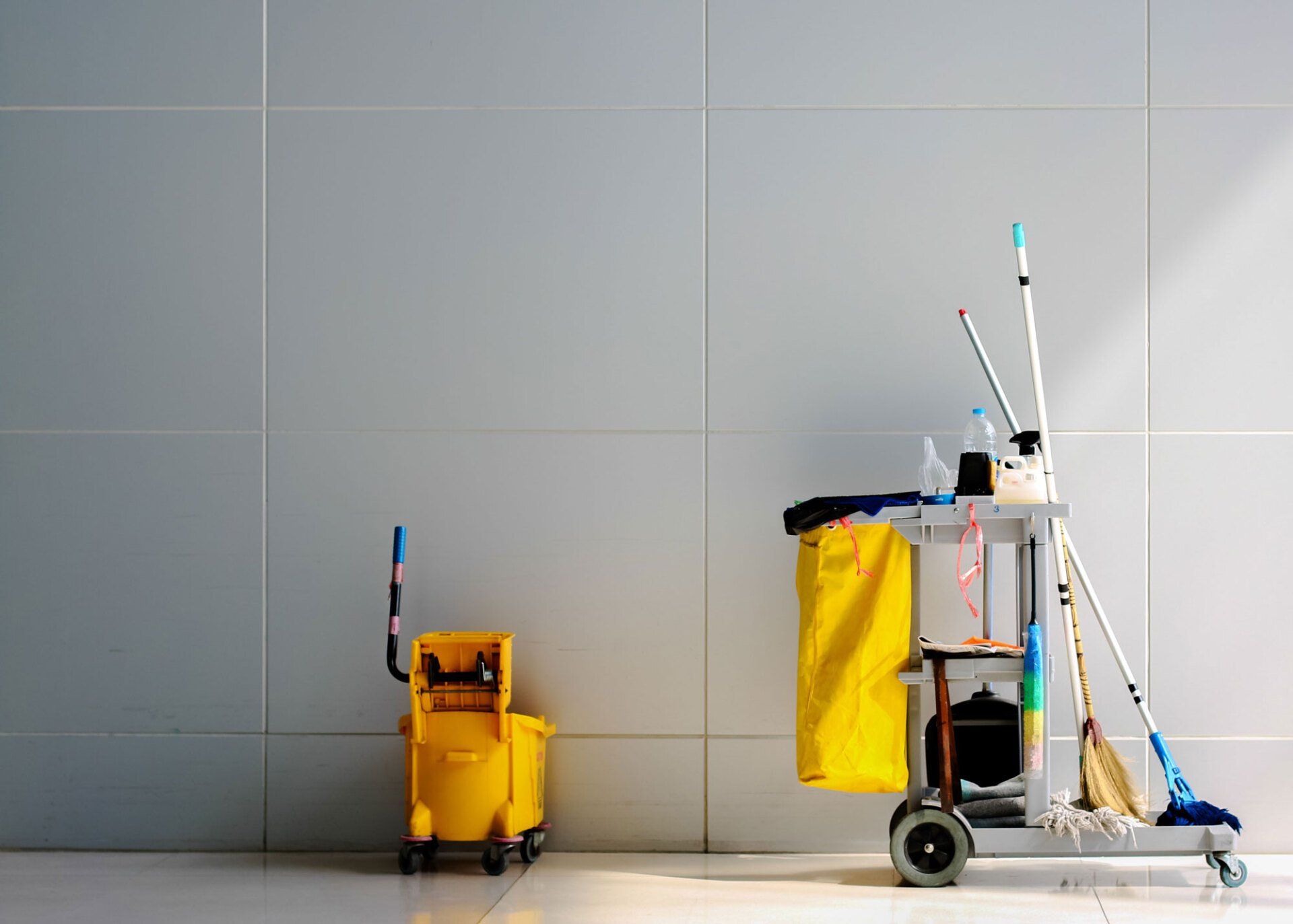 A yellow mop bucket and a cleaning cart with cleaning supplies on a tiled floor.
