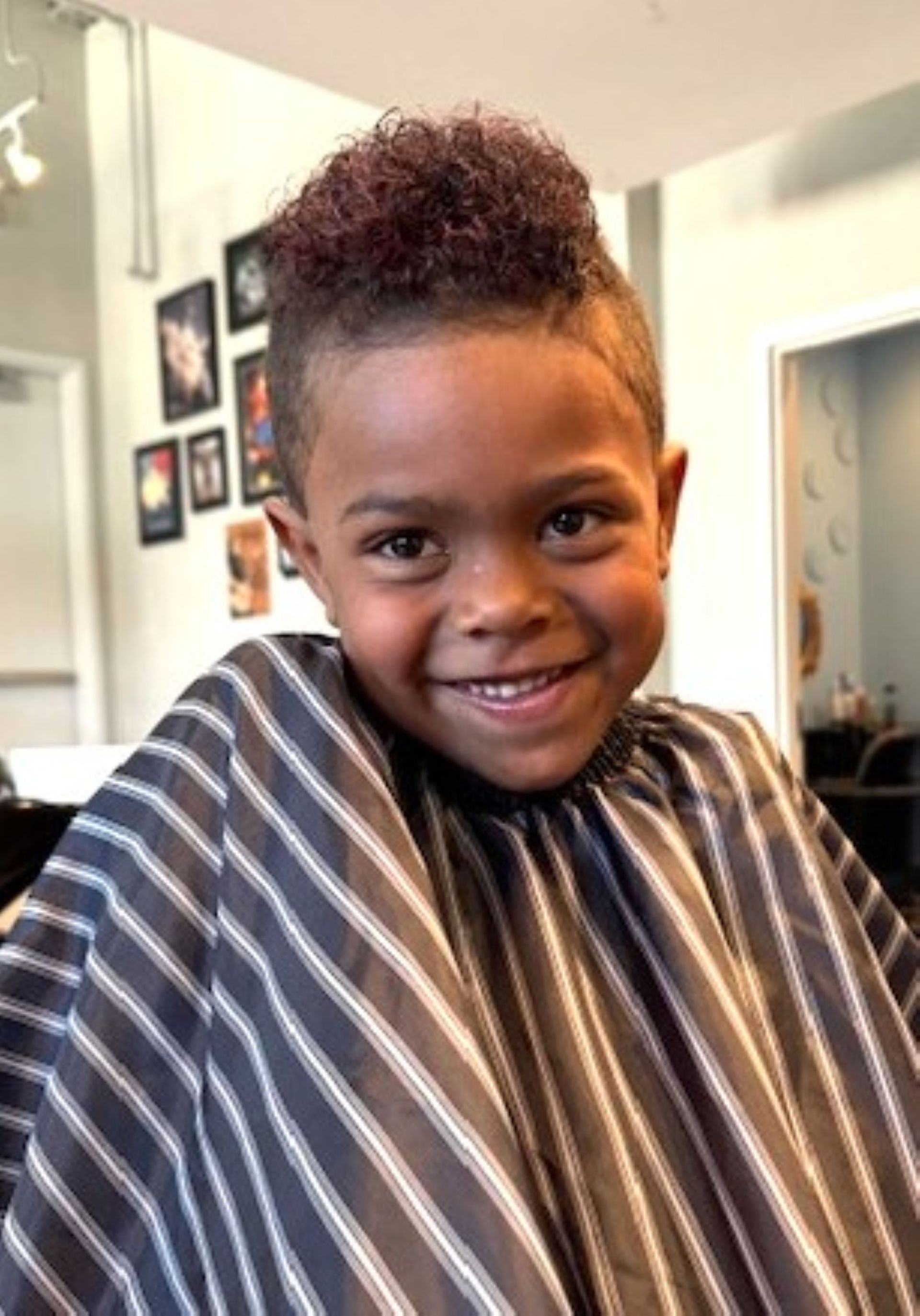 A young boy is getting his hair cut at a barber shop and smiling.