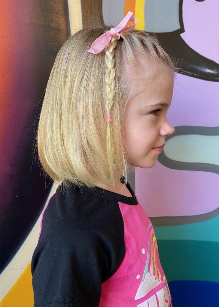 A little girl with blonde hair is wearing a pink bow in her hair.