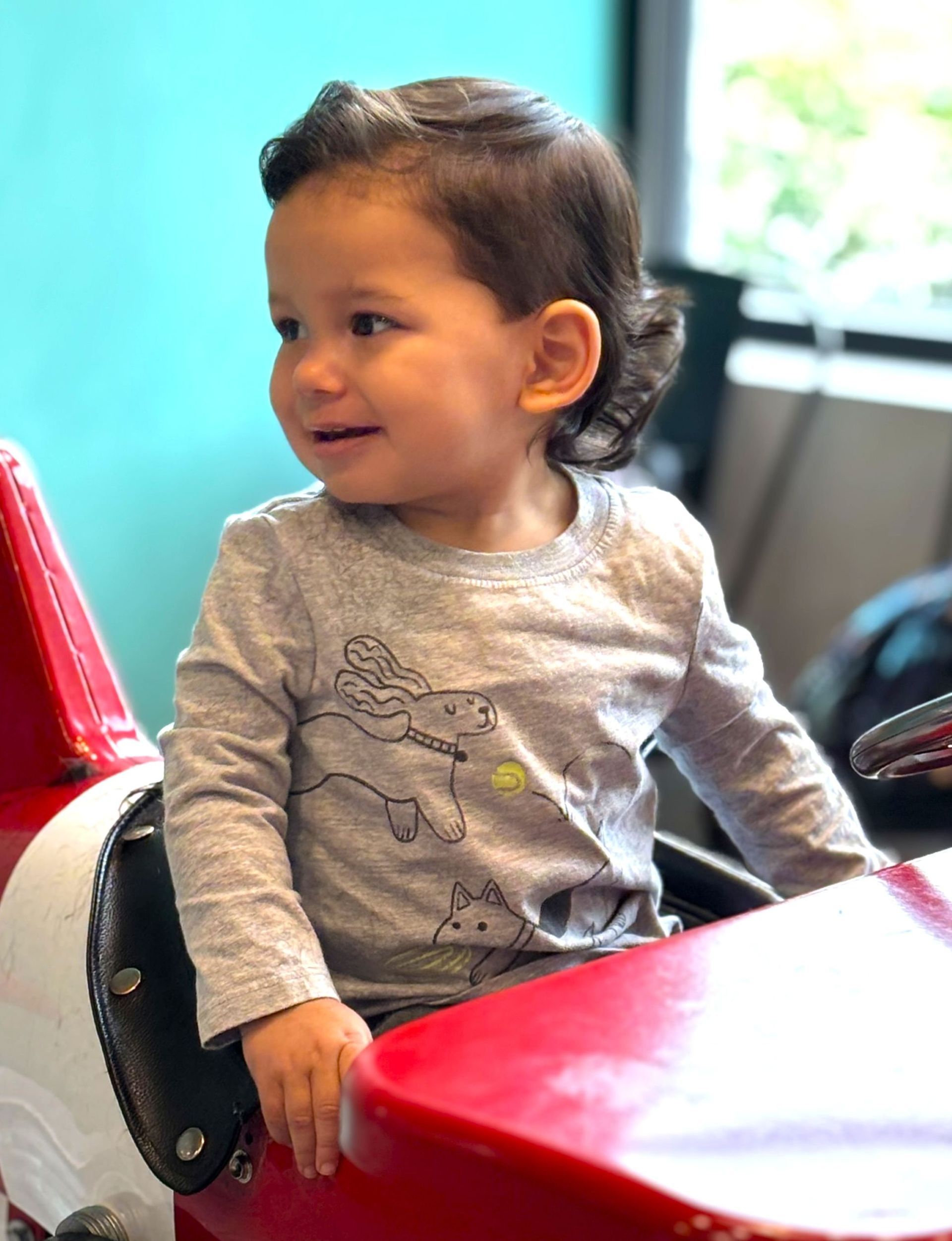 A little boy is sitting in a red toy car.