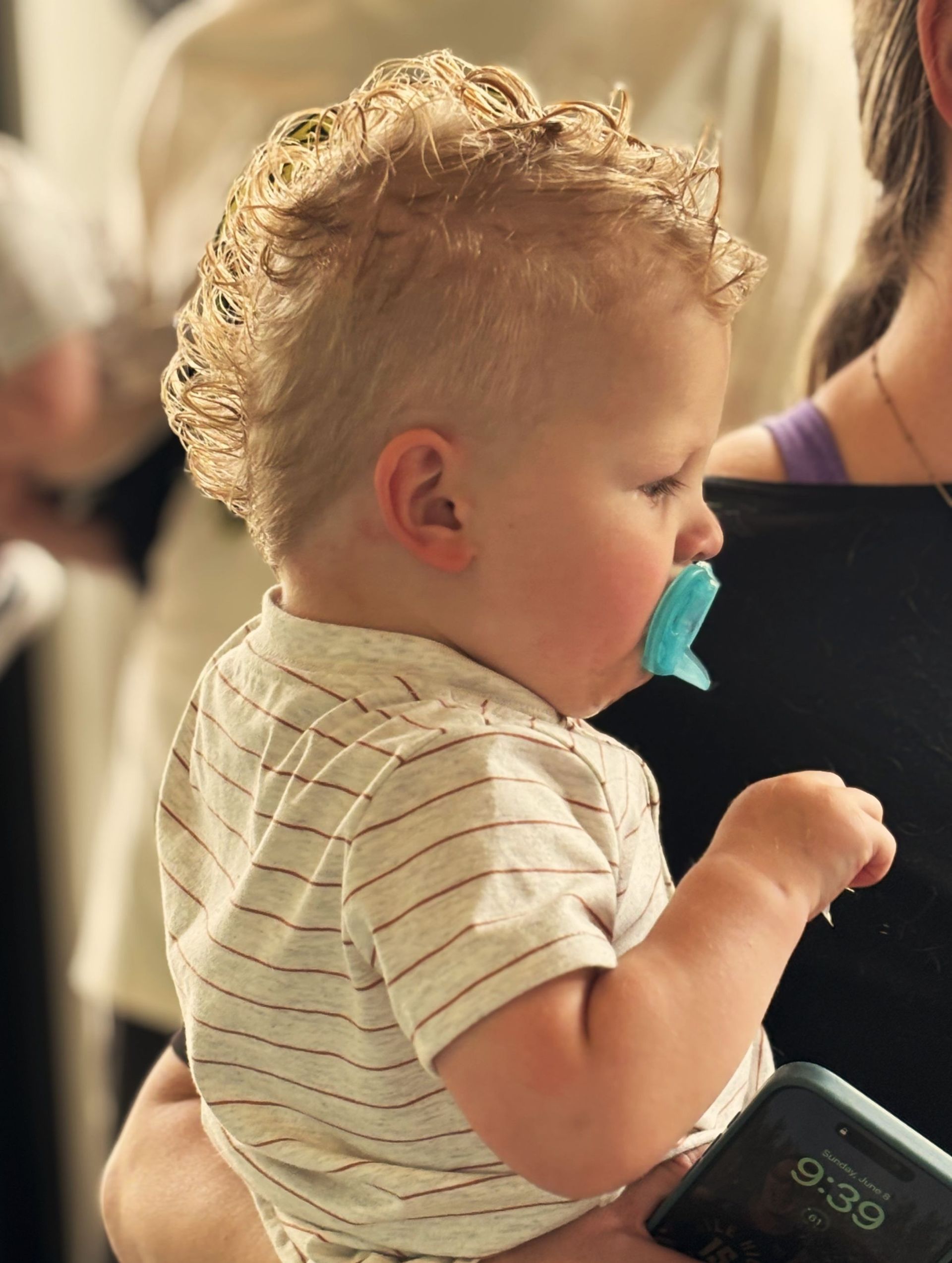 A baby with a pacifier in his mouth is being held by a woman.