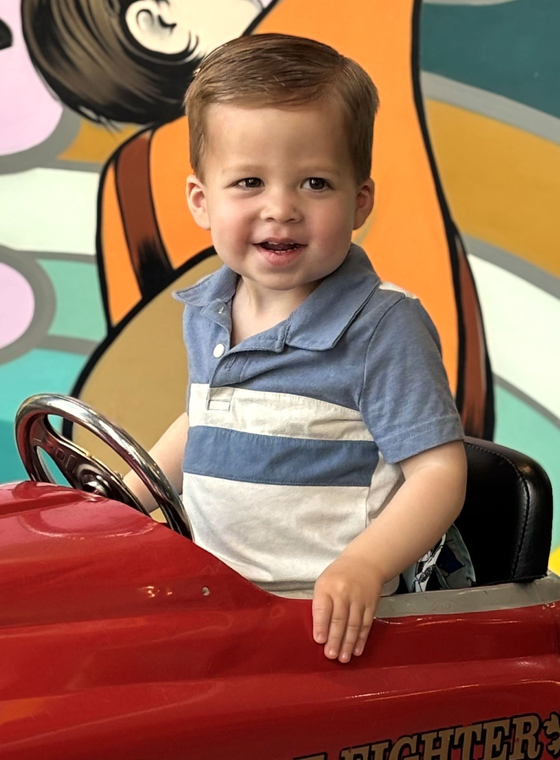 A young boy is sitting in a red toy car.