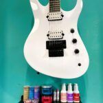 A white electric guitar is sitting on top of a table next to bottles of nail polish.