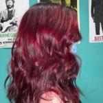 A woman with red hair is standing in front of a blue wall.