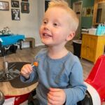 A little boy is sitting in a chair at a barber shop holding a lollipop.