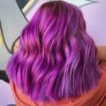 A woman with purple hair is standing in front of a purple wall.