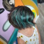 A little girl with green hair is standing in front of a colorful wall.
