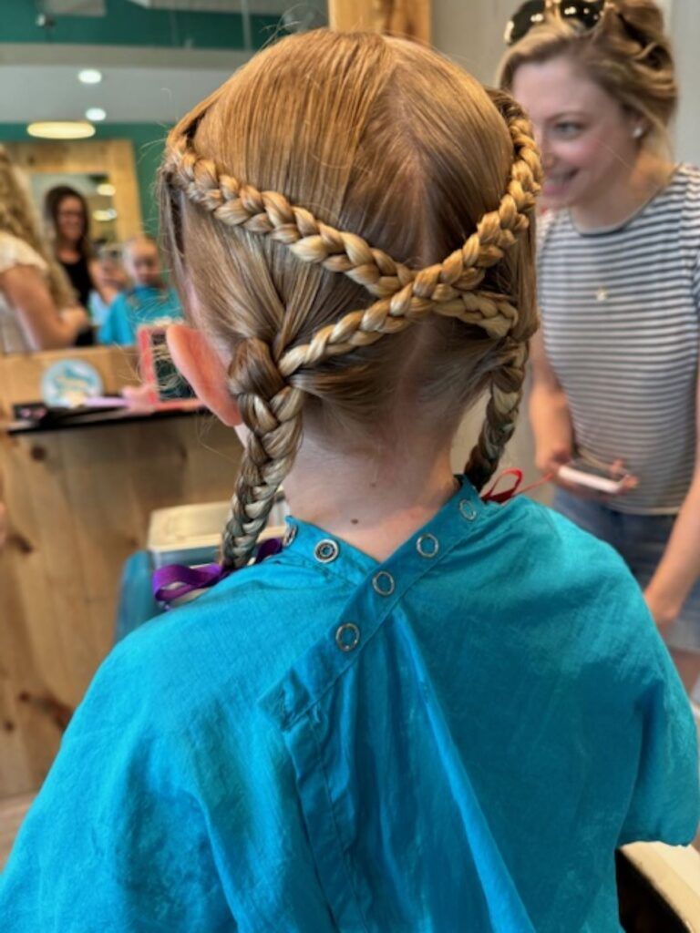 A little girl is getting her hair braided in a salon.