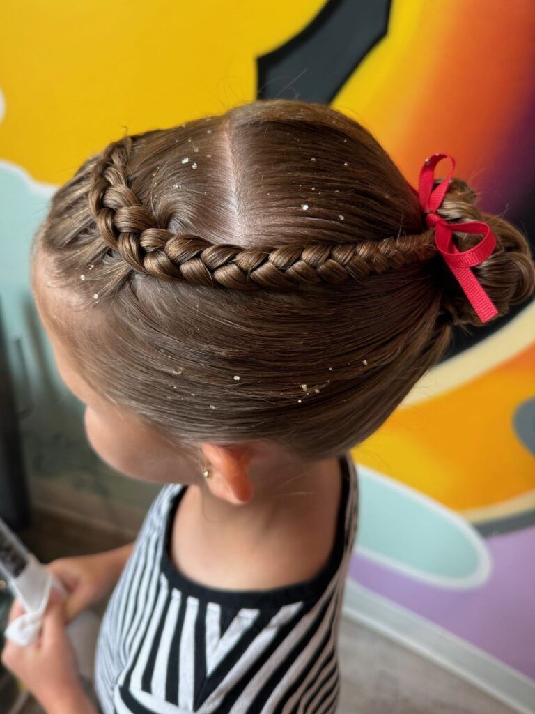 A little girl is wearing a braided bun with a red bow.