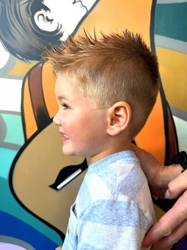 A little boy is getting his hair cut in front of a graffiti wall.