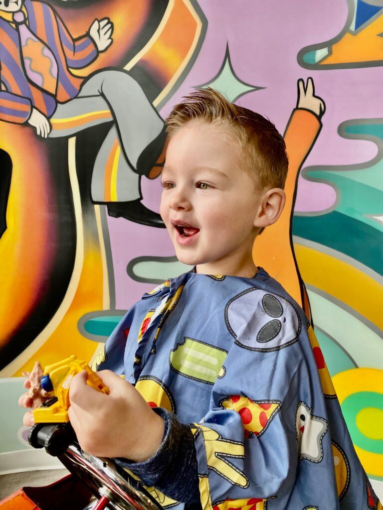 A little boy is getting his hair cut in front of a graffiti wall.