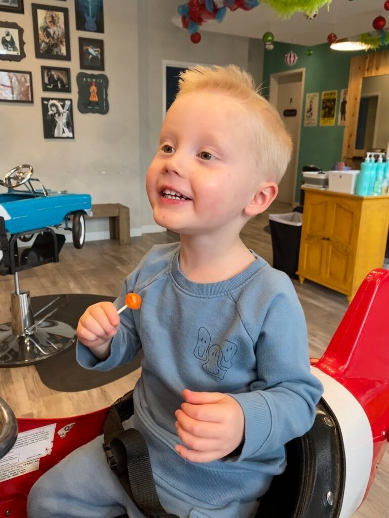 A little boy is sitting in a chair holding a lollipop.