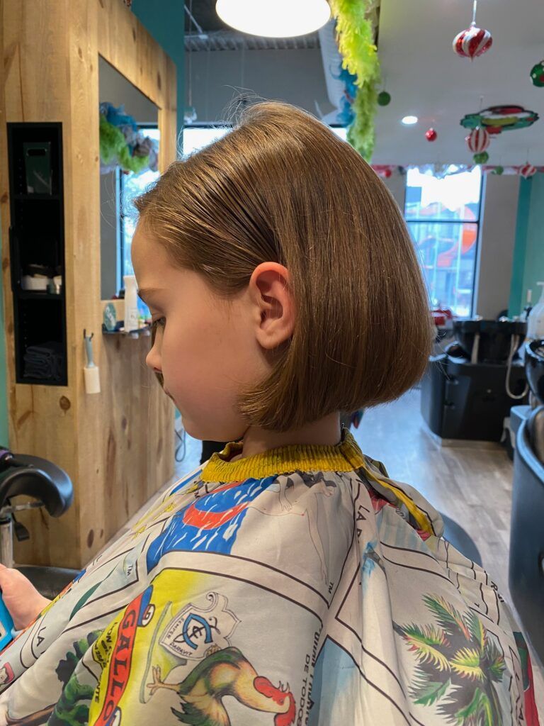 A little girl is getting her hair cut at a barber shop.