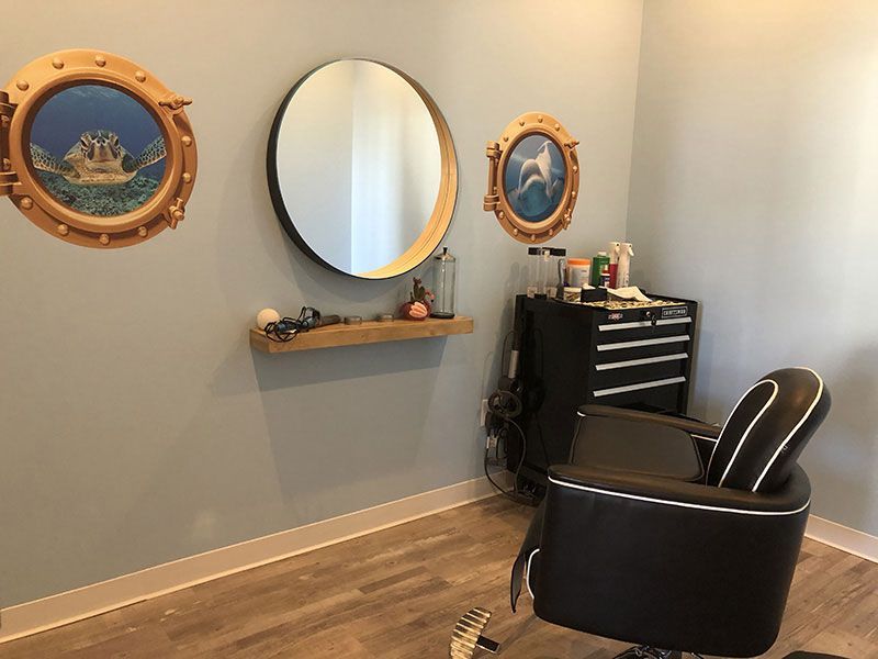 A hair salon with a chair , mirrors and paintings on the wall.