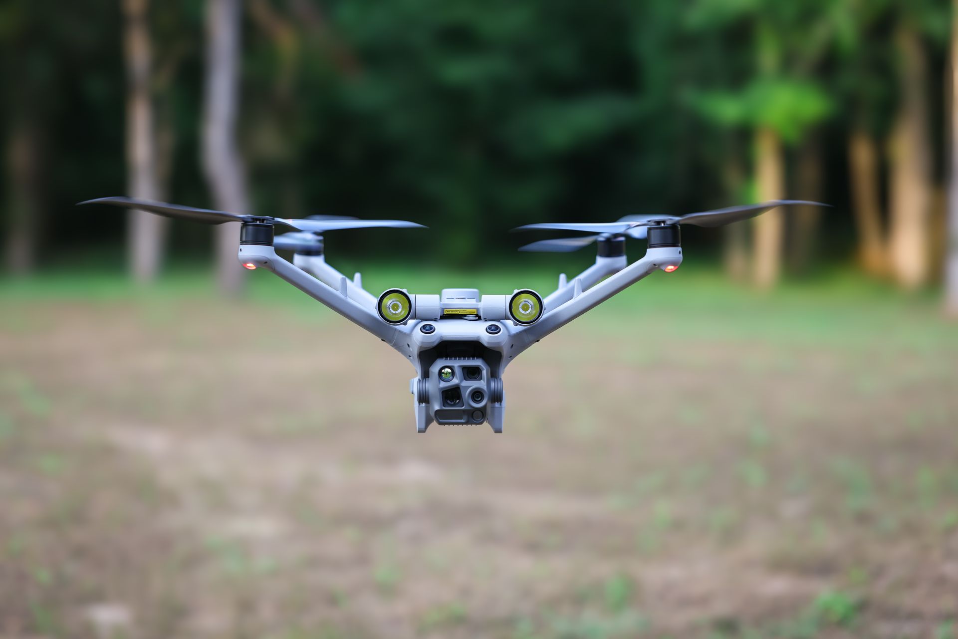 Drone flying outdoors in a blurred wooded area, centered with propellers visible.