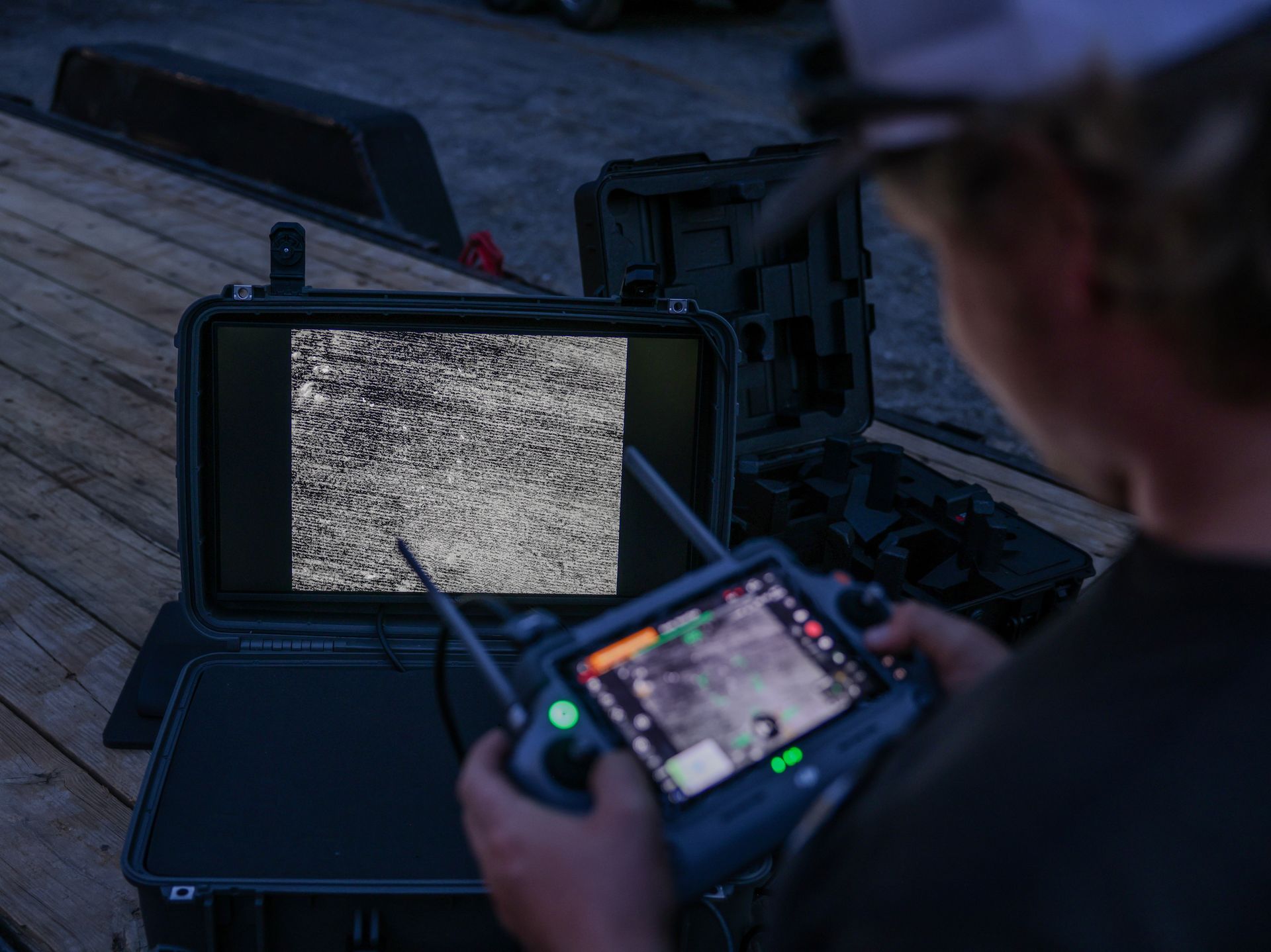 Person operating a drone controller beside a screen with static at dusk