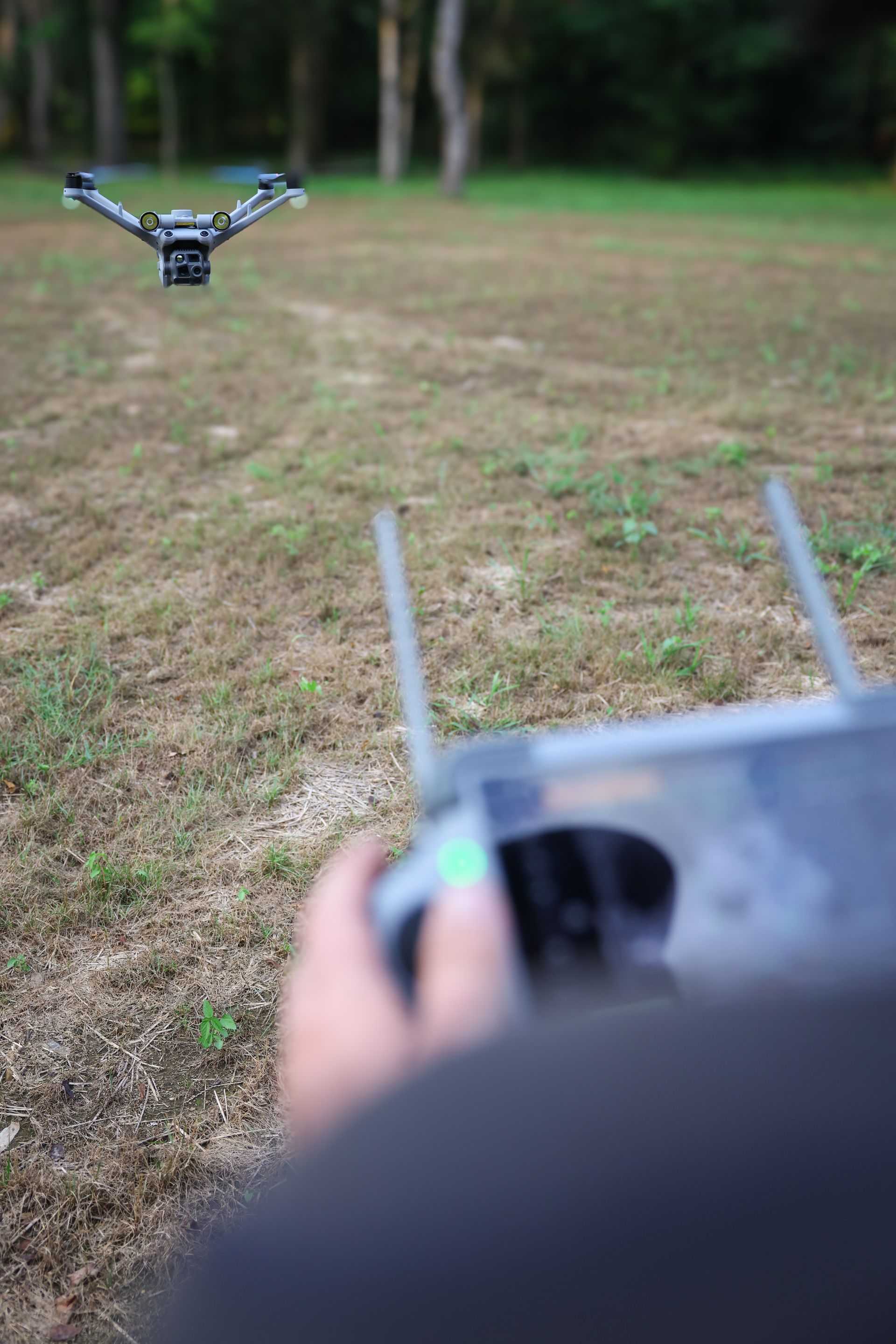 Handheld drone controller aiming a small drone flying low over a grassy field
