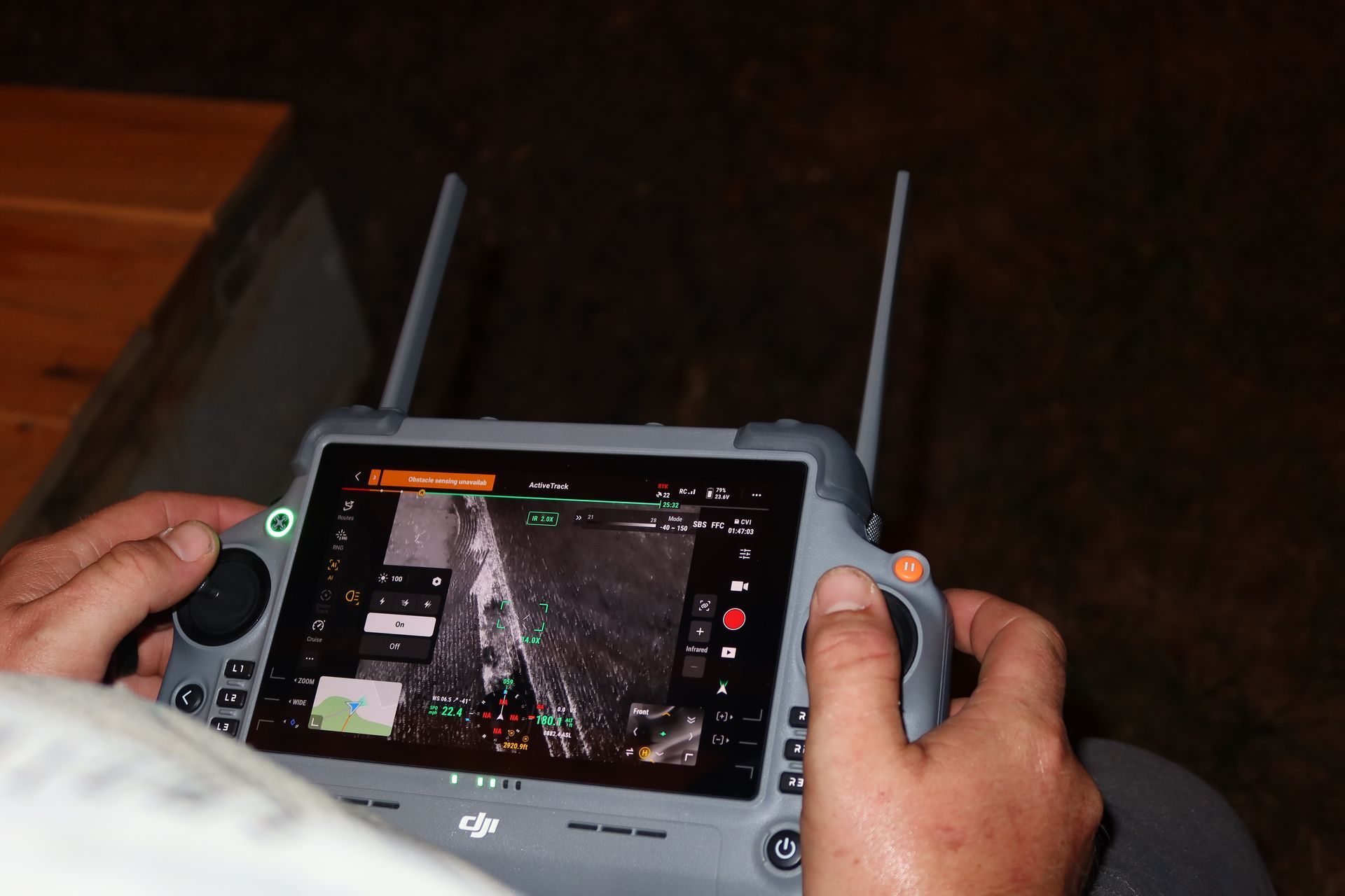 Hands holding a drone controller with a tablet displaying a live aerial view.