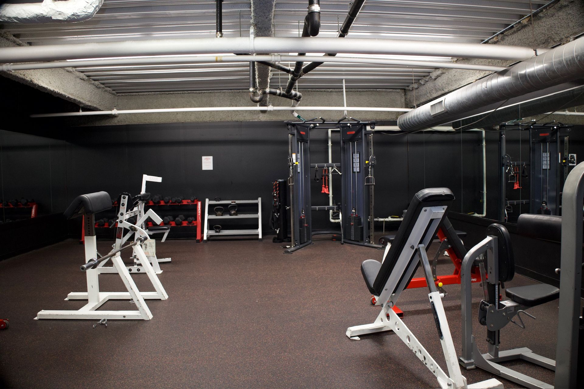 Gym interior with exercise equipment on a rubber floor; includes weight racks, weight machines, and a pull-up bar.