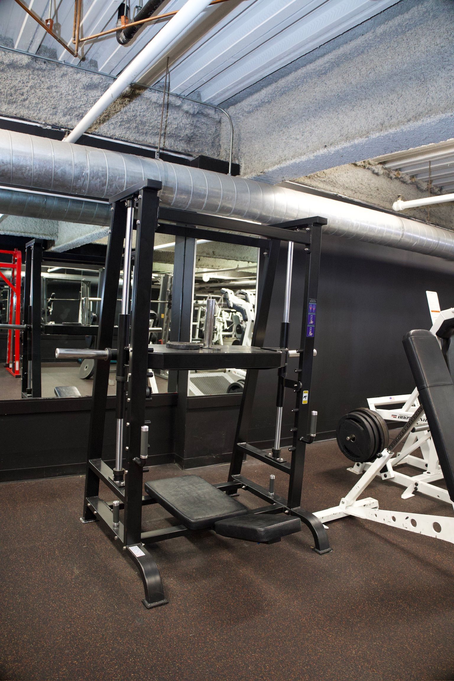 A black weight machine in a gym. Bench attached. Other equipment in the background.