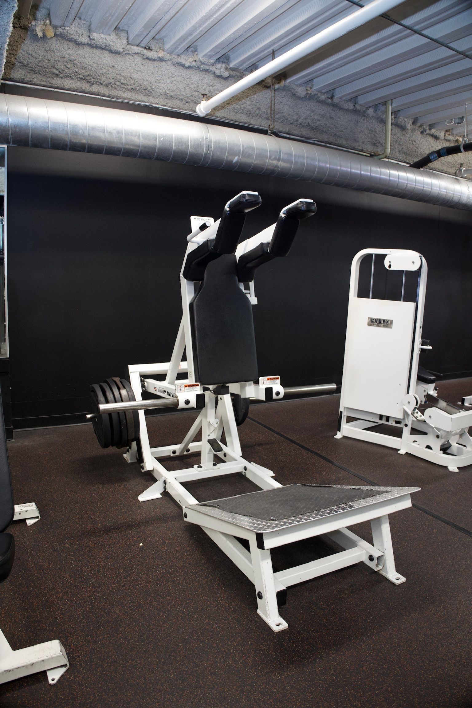 A weight machine in a gym, designed for leg exercises, with black padding, a white frame, black floor.