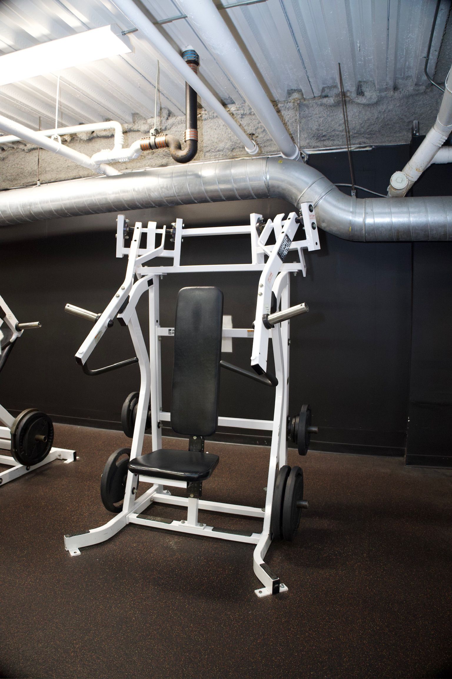 Weight machine in a gym, white frame, black padding, black weights on pegs.