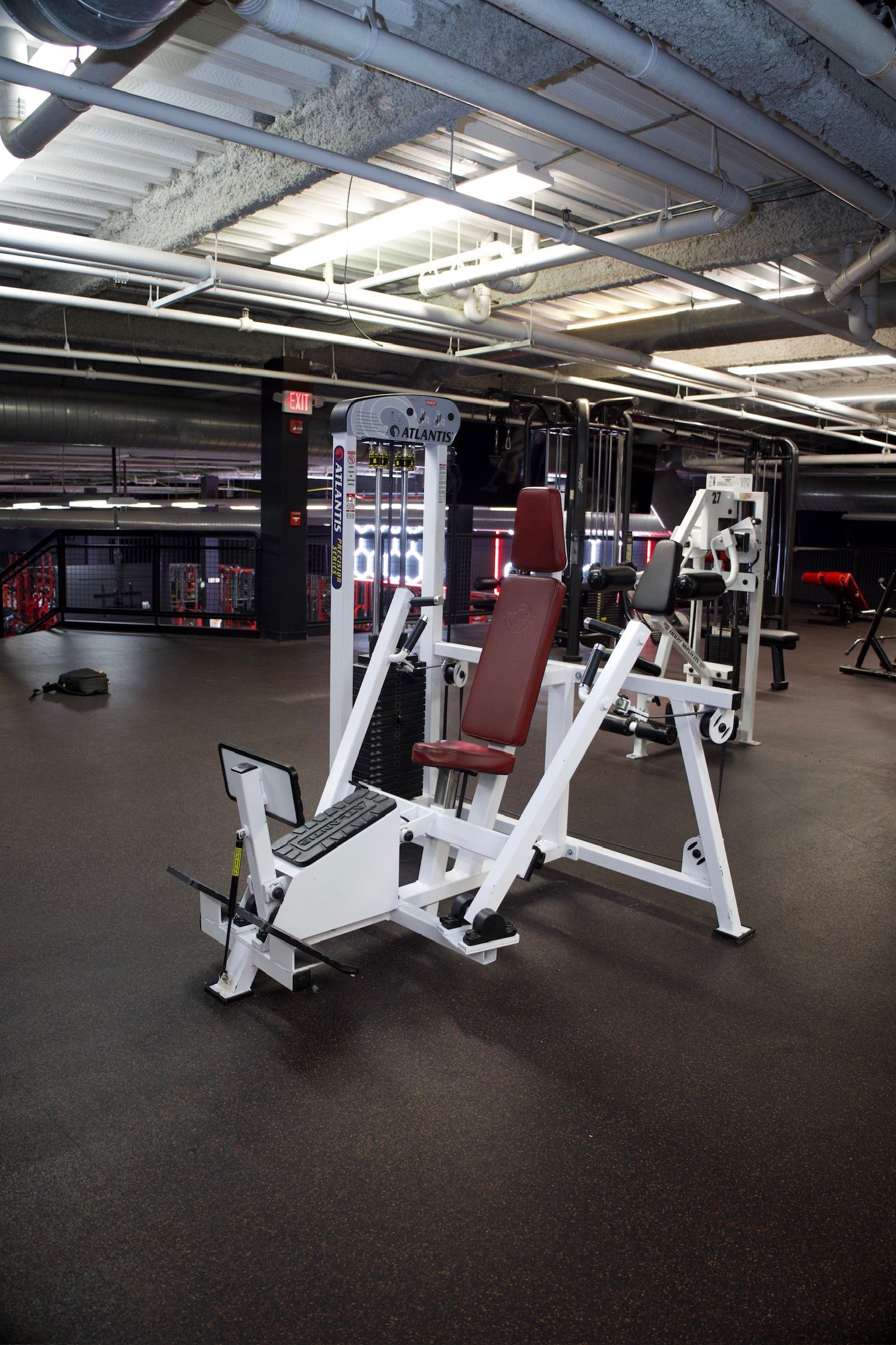 Weight machine in a gym, white and red, with black floor and industrial ceiling.