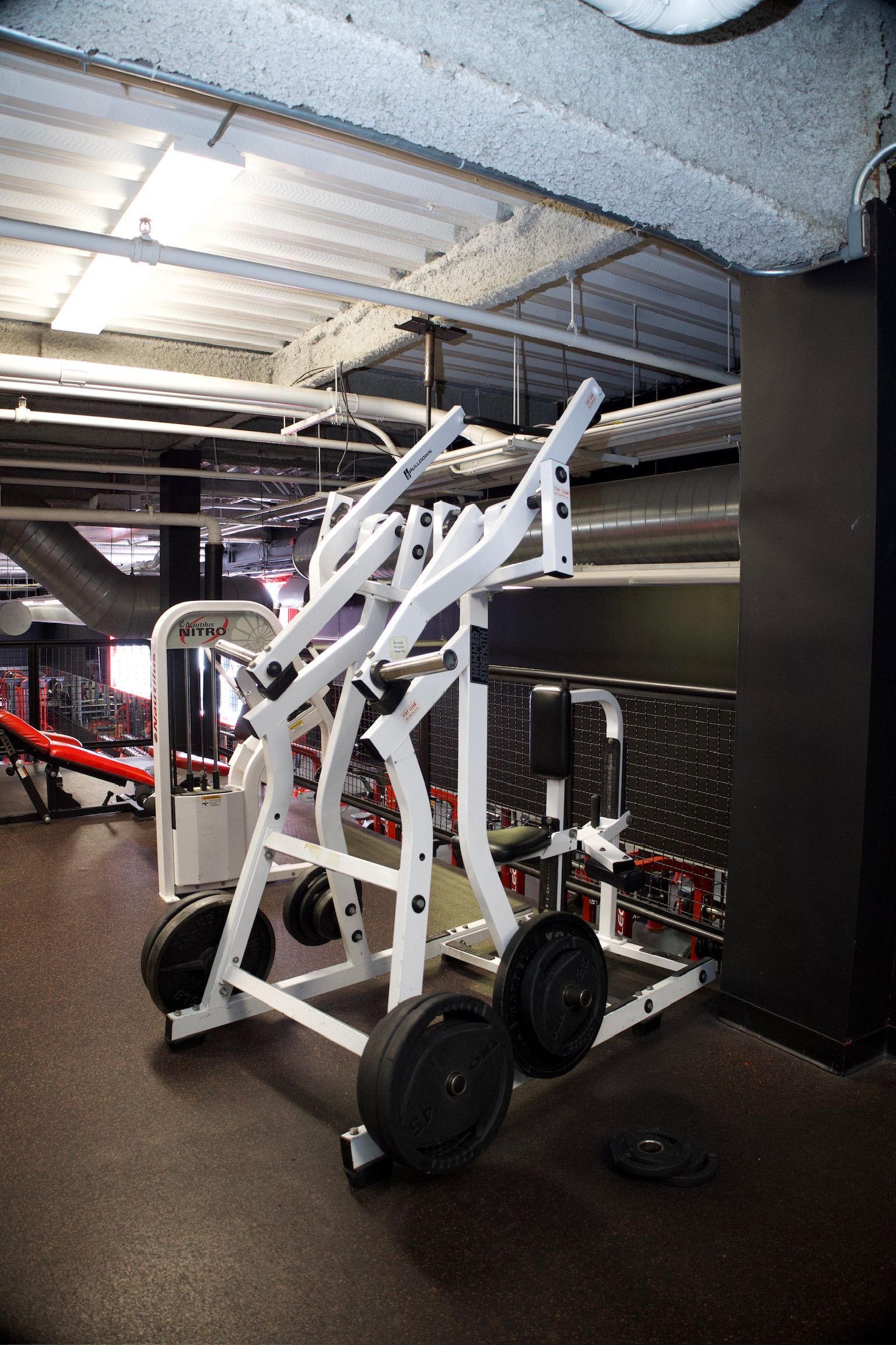 White lever gym machine with weight plates on a black gym floor.