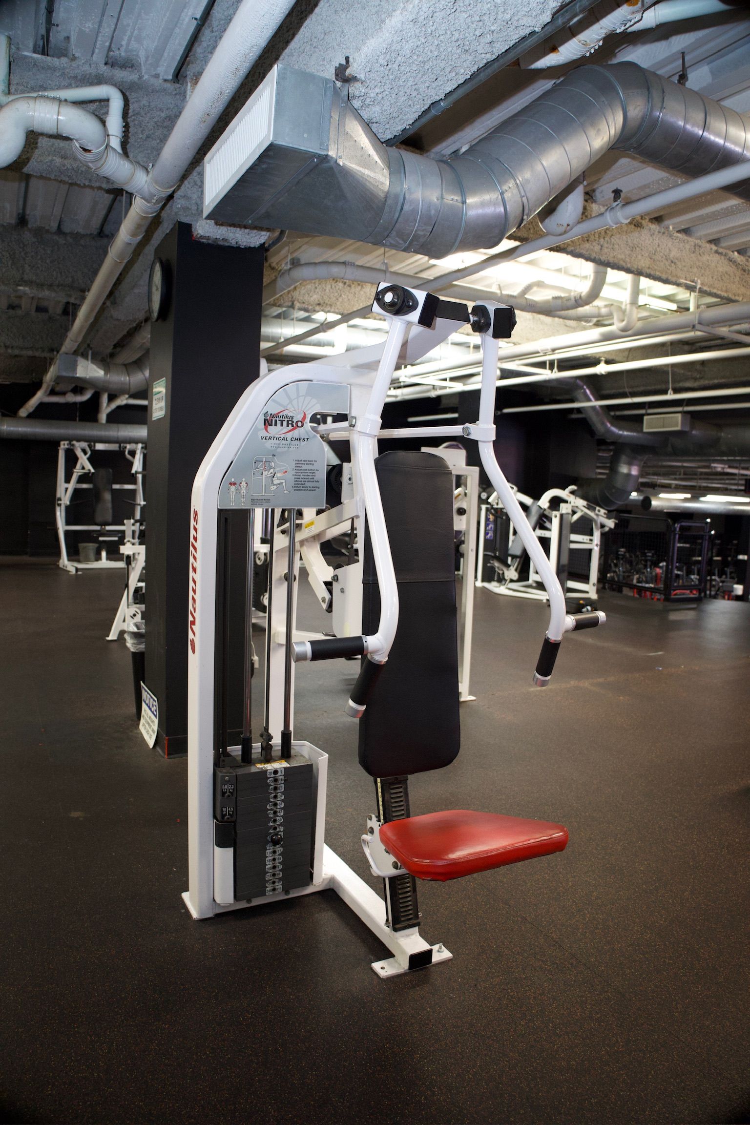 Chest press machine in a gym setting. The machine is white, black, and red.
