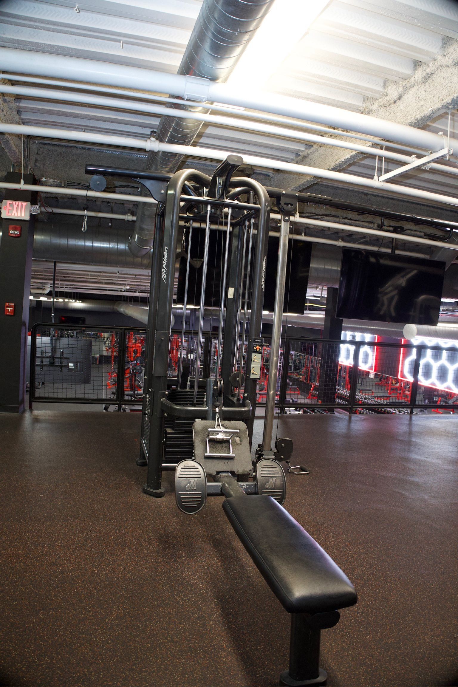 A weight machine in a gym setting with black rubber flooring and a bench.