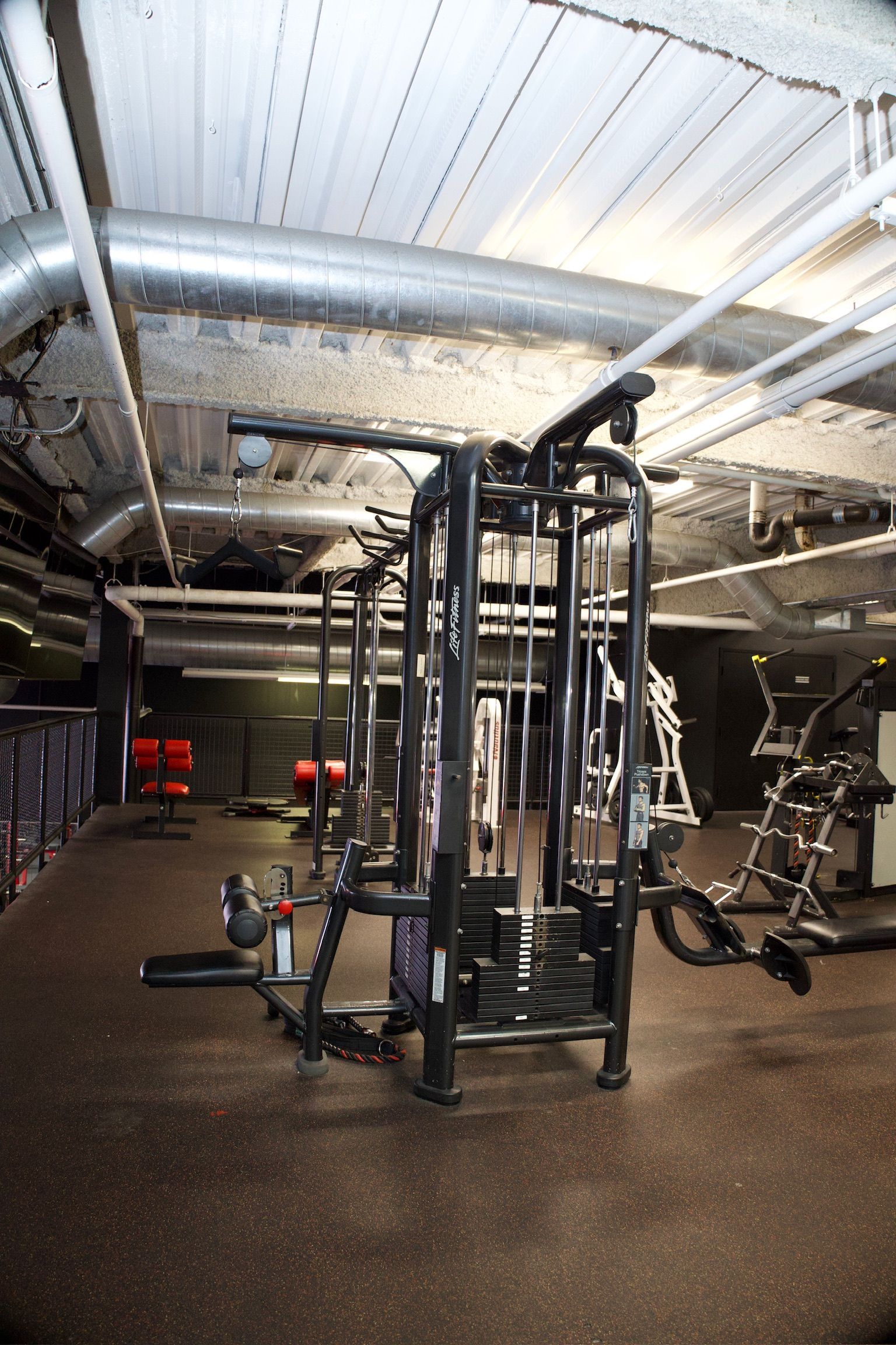 Gym interior with weight machines, dark floors, and exposed ceiling ductwork.
