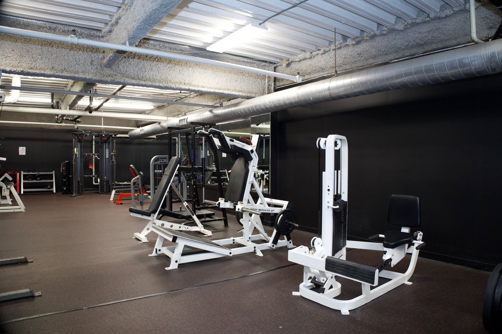 Gym interior with various exercise machines, dark walls, and a light-colored ceiling.
