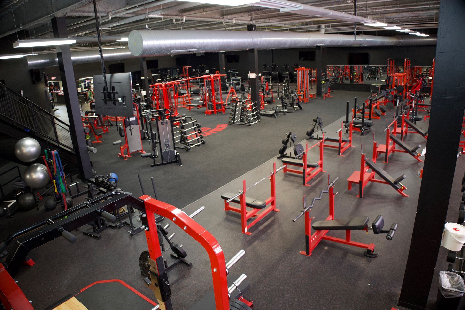 A large, well-equipped gym with red weight machines and black flooring.