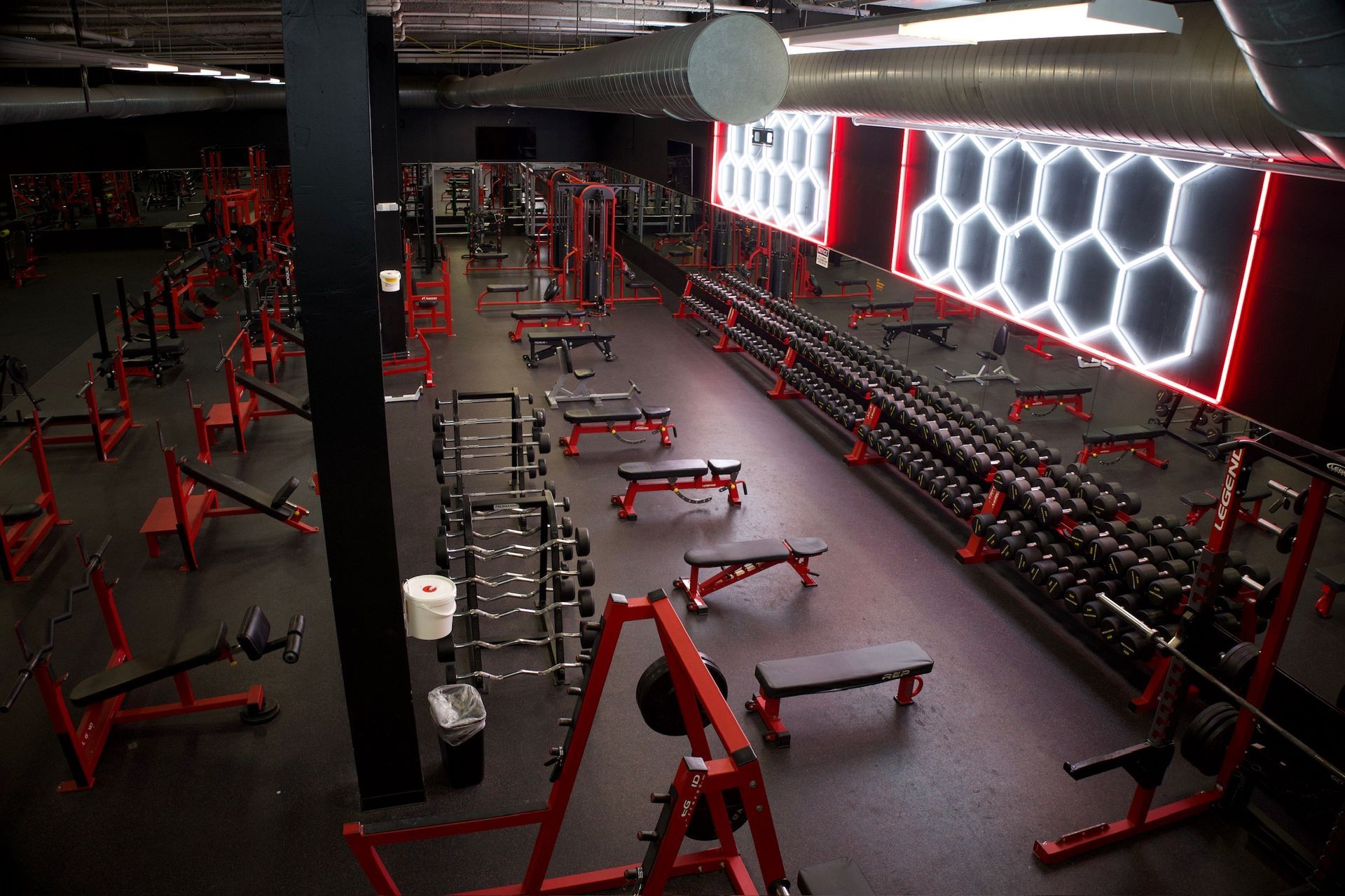 Gym interior with red equipment, weights, mirrors, and a hexagonal light fixture.