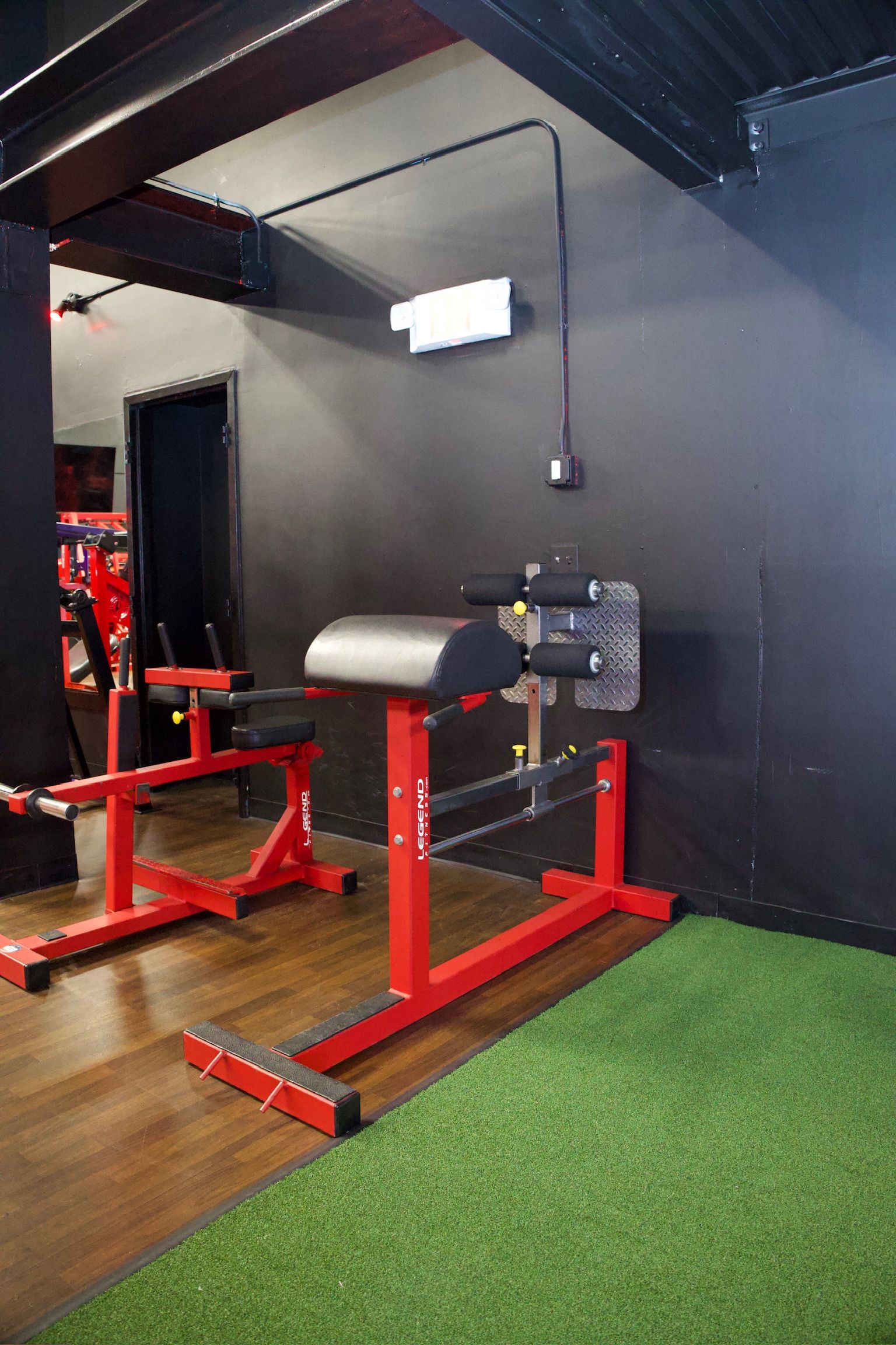 Red and black gym equipment against a black wall. Green turf flooring.