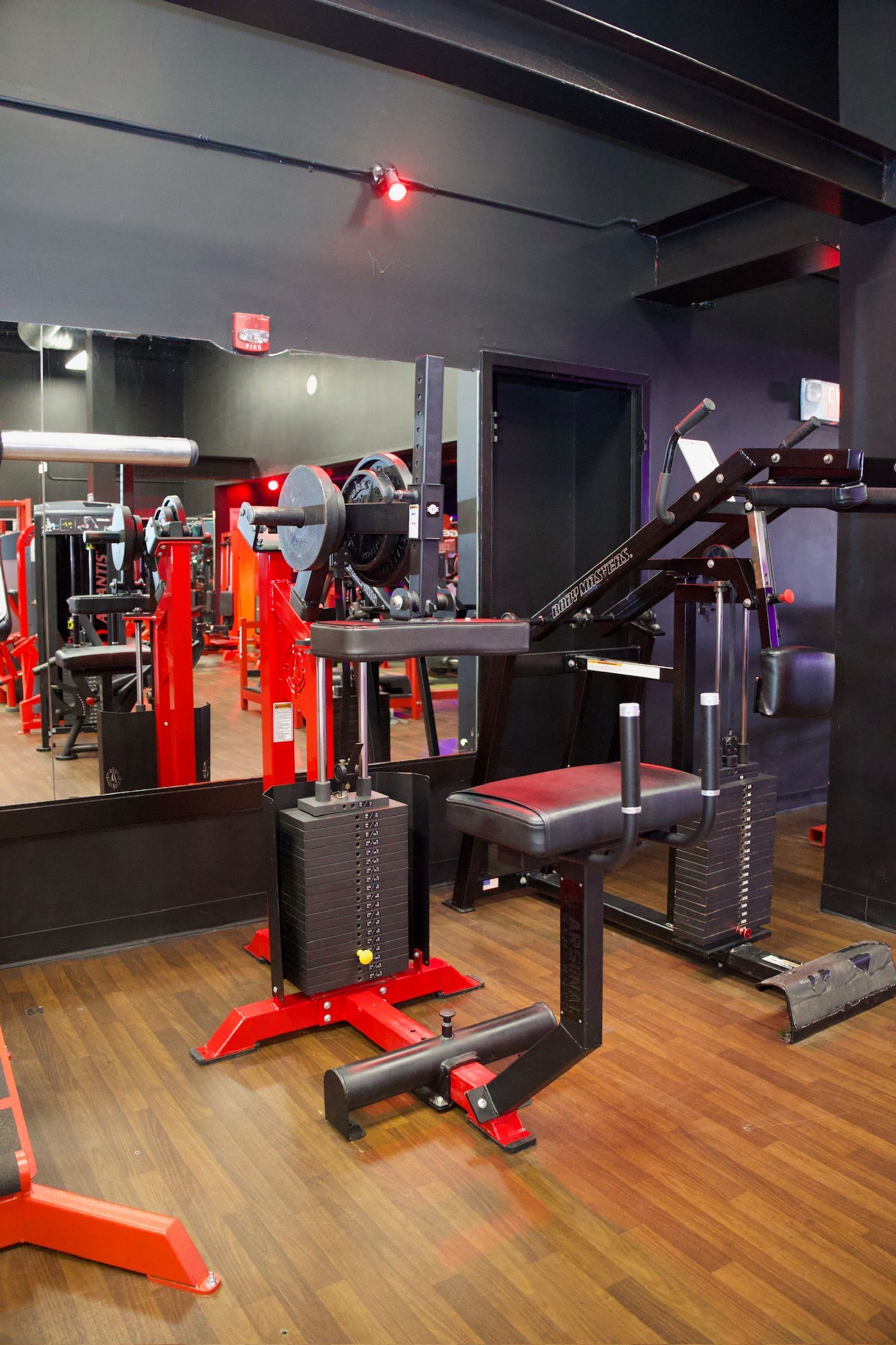 Weightlifting equipment in a gym with red and black accents and dark wood floors.