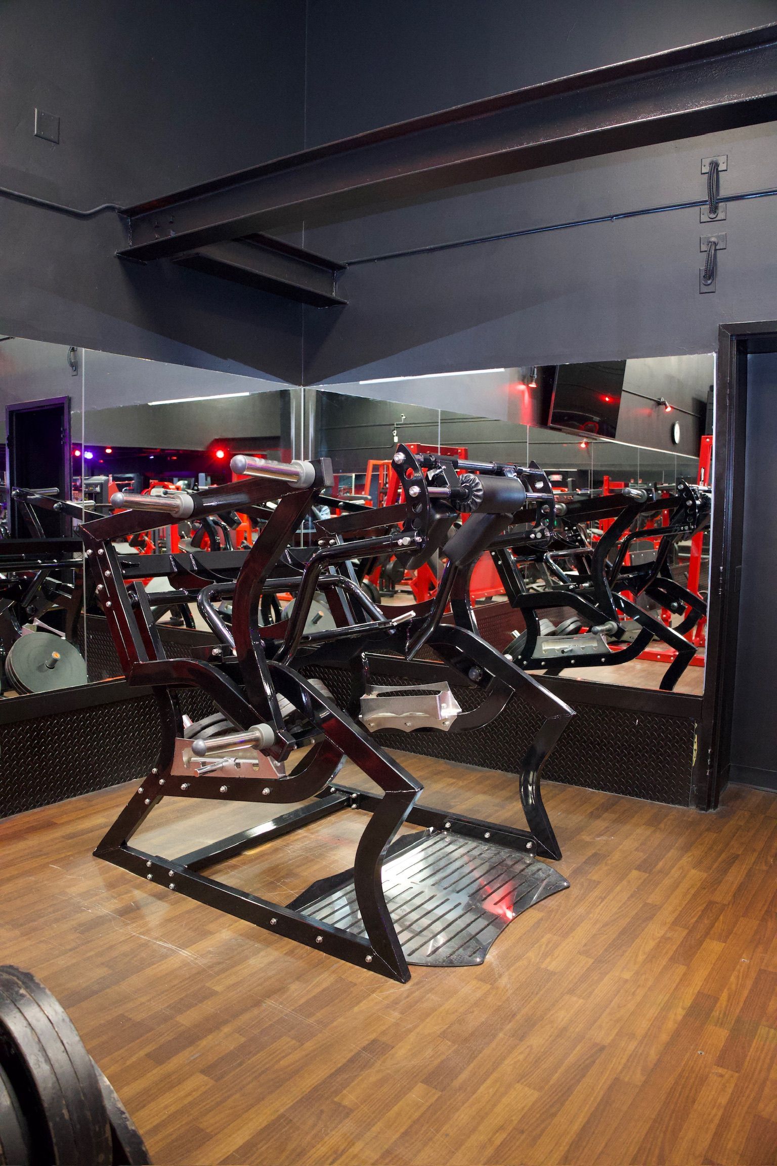 Gym interior with exercise equipment, wood floor, and mirrors. Black and red accents.