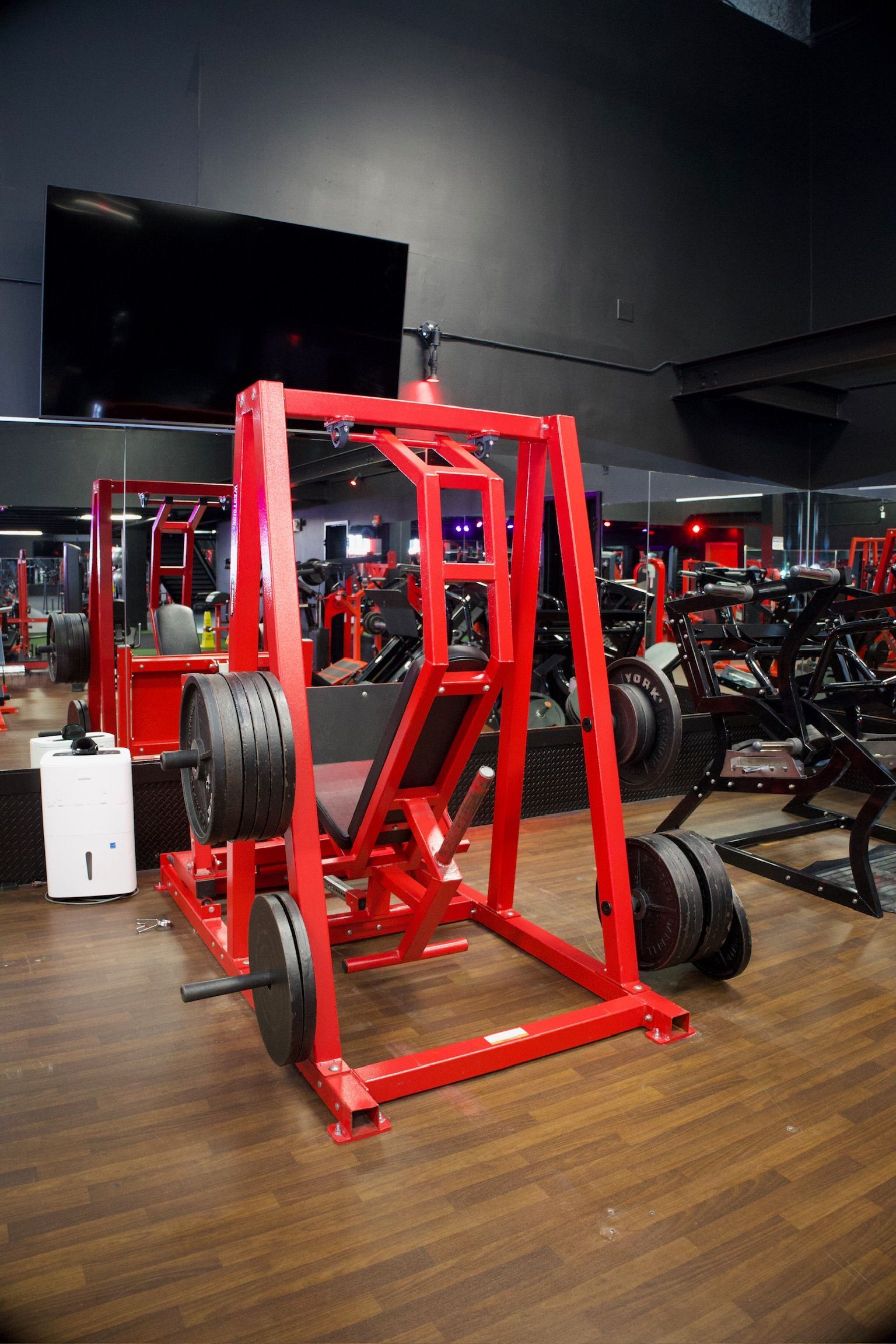 Red leg press machine with weight plates in a gym.