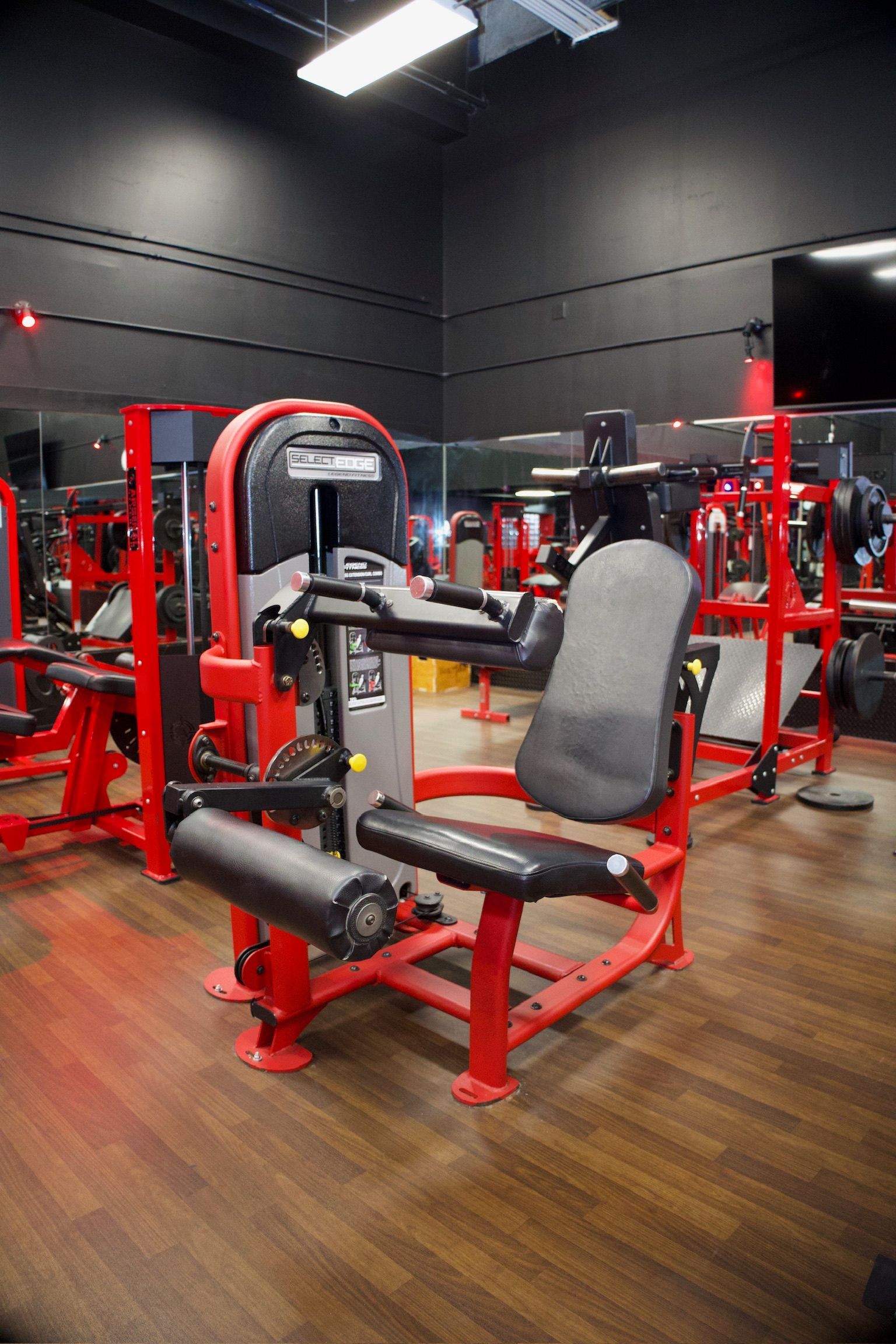 Red and black leg extension machine in a gym setting, other equipment visible.