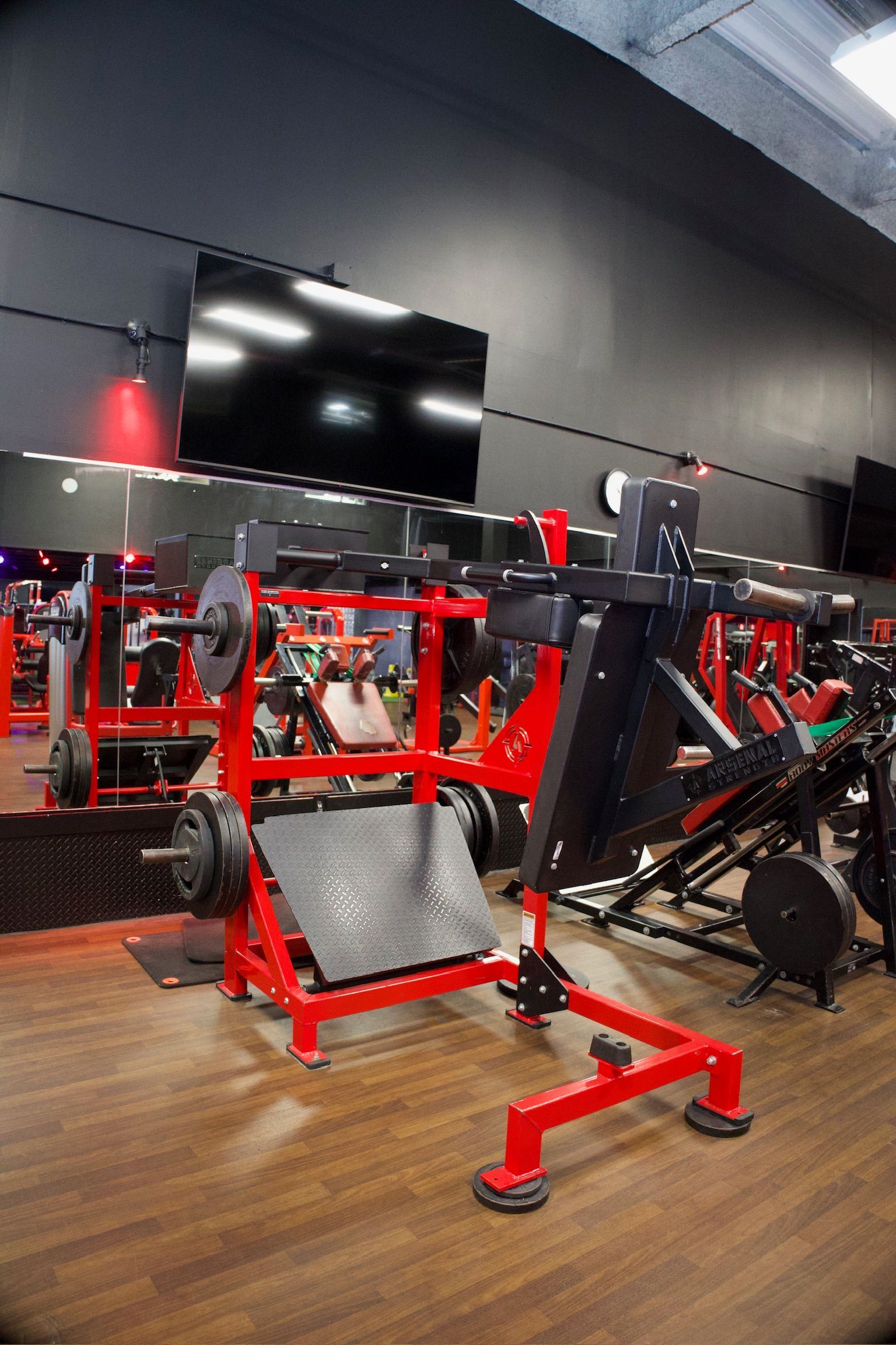 Red weightlifting machine in a gym with weights, TV on the wall, and other exercise equipment.