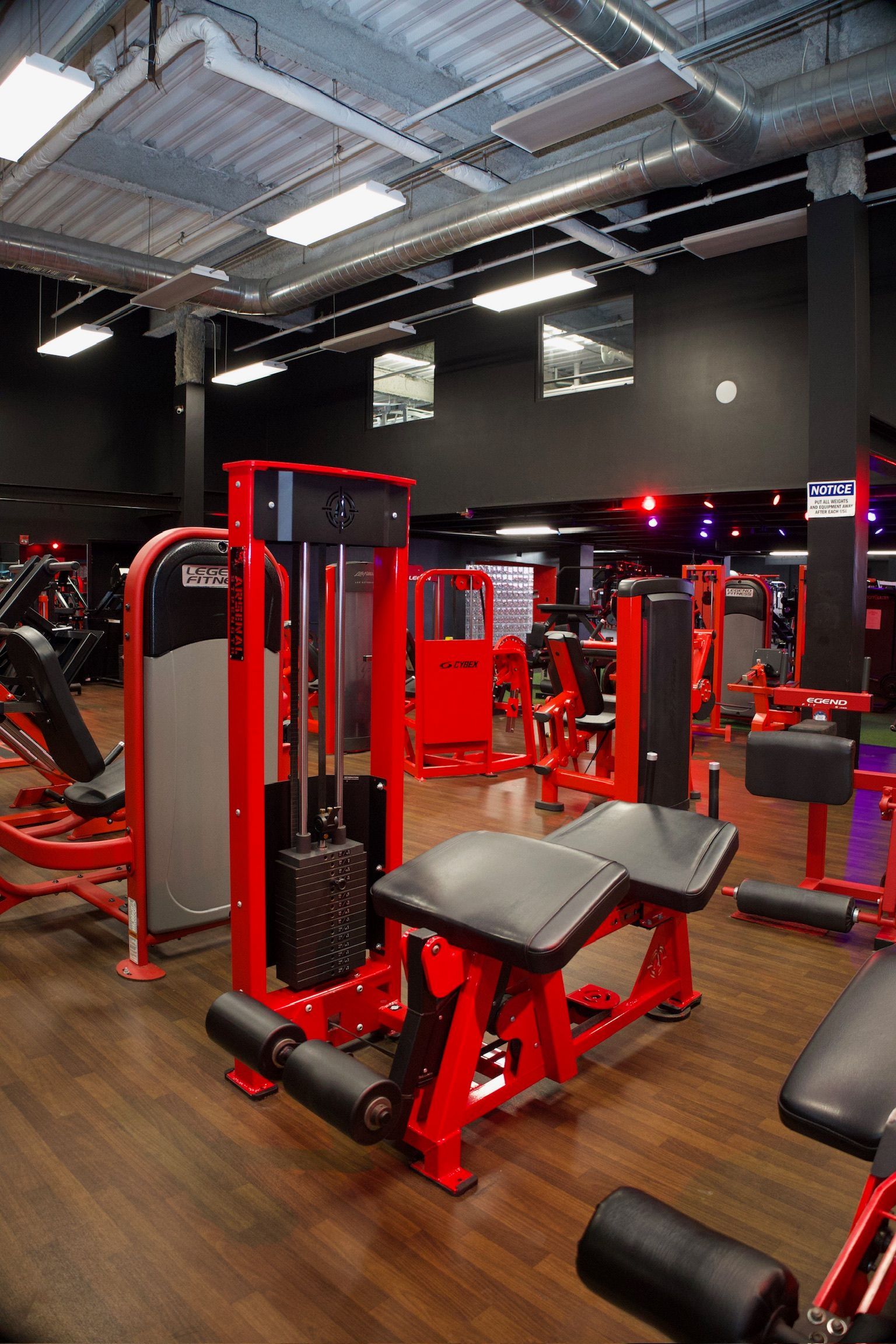Red gym equipment in a fitness center with dark walls and wood flooring.