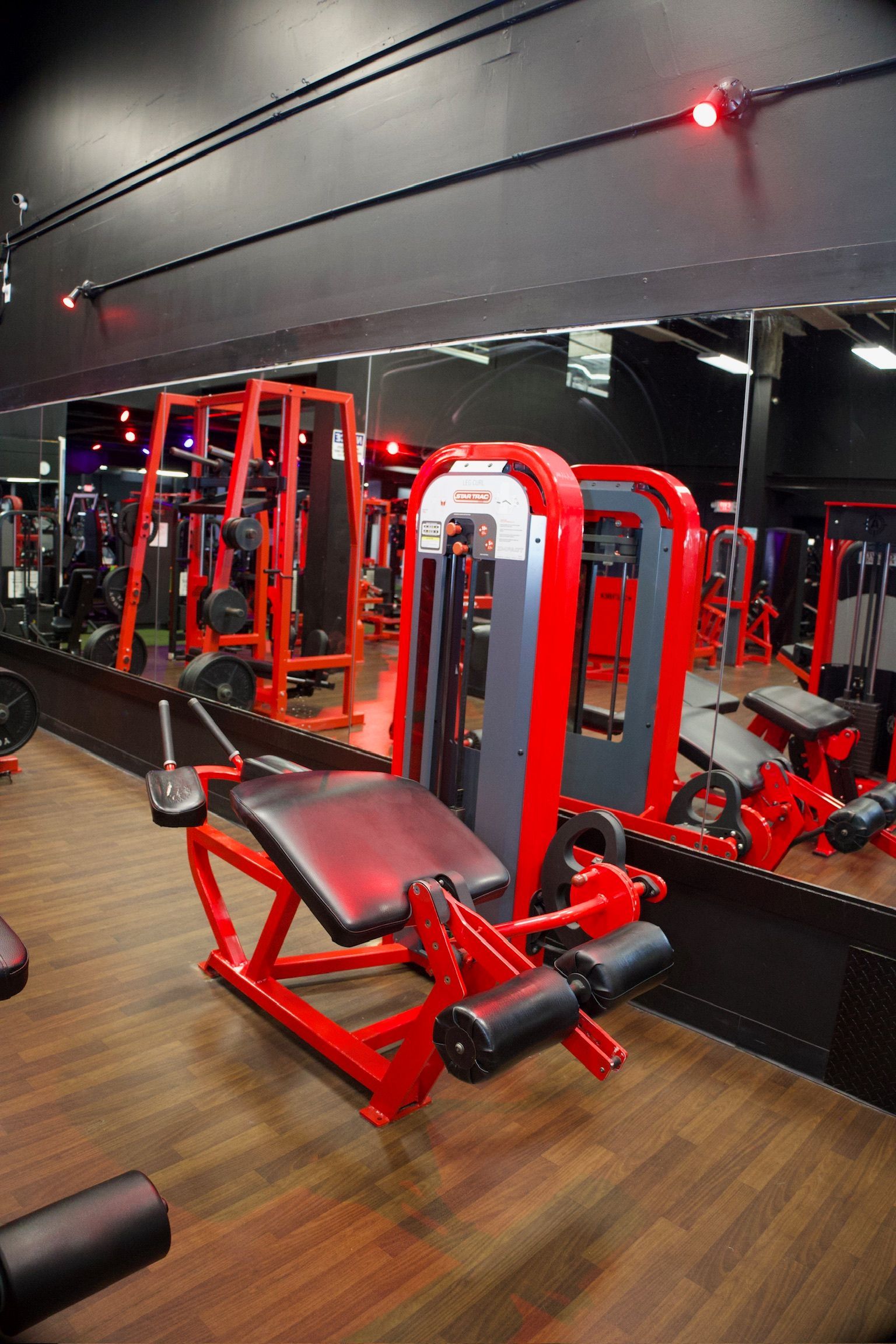 Red and gray leg extension machine in a gym with other weight machines and a large mirror.