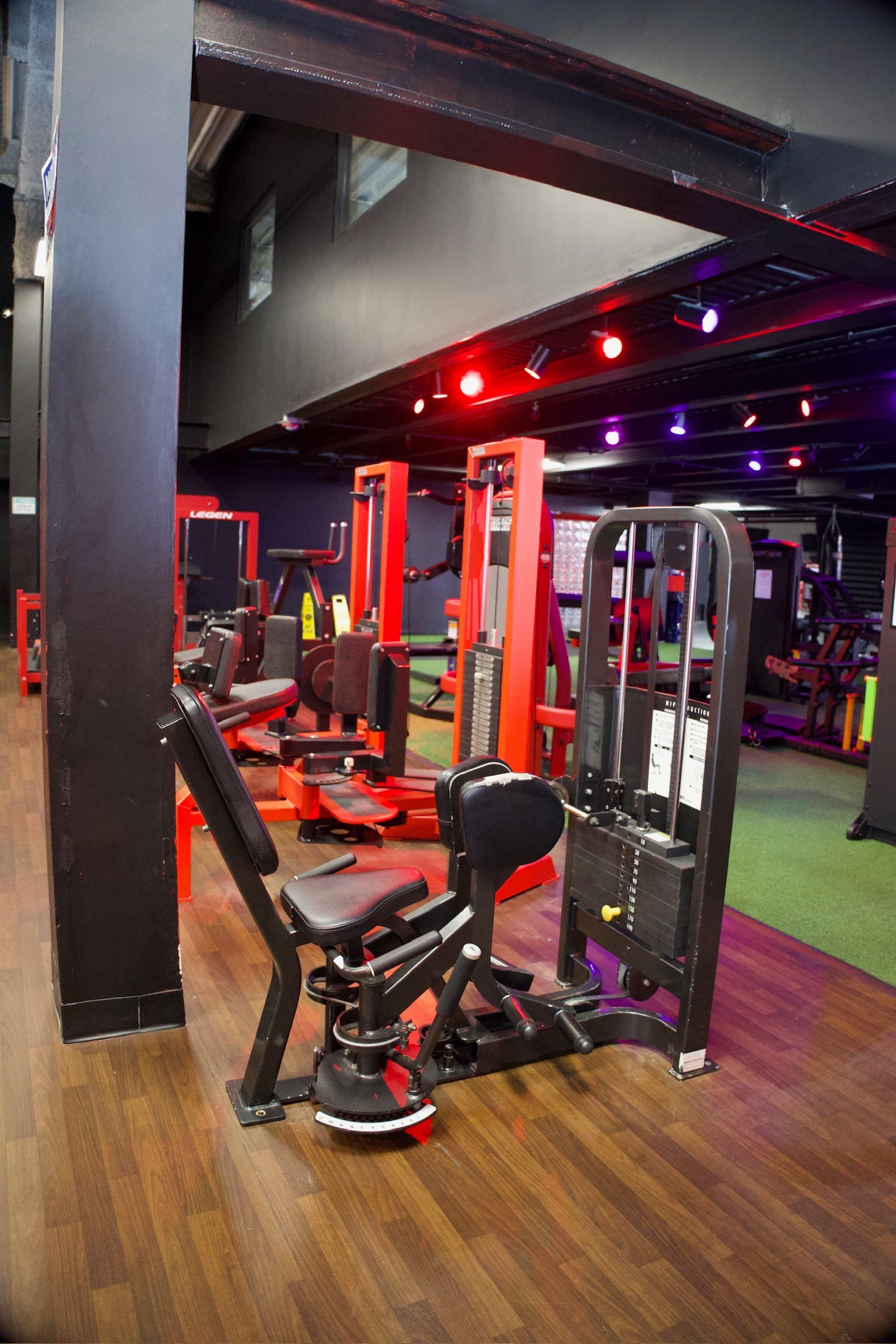 Gym interior with various exercise machines, a black and red color scheme, wood flooring, and overhead lighting.