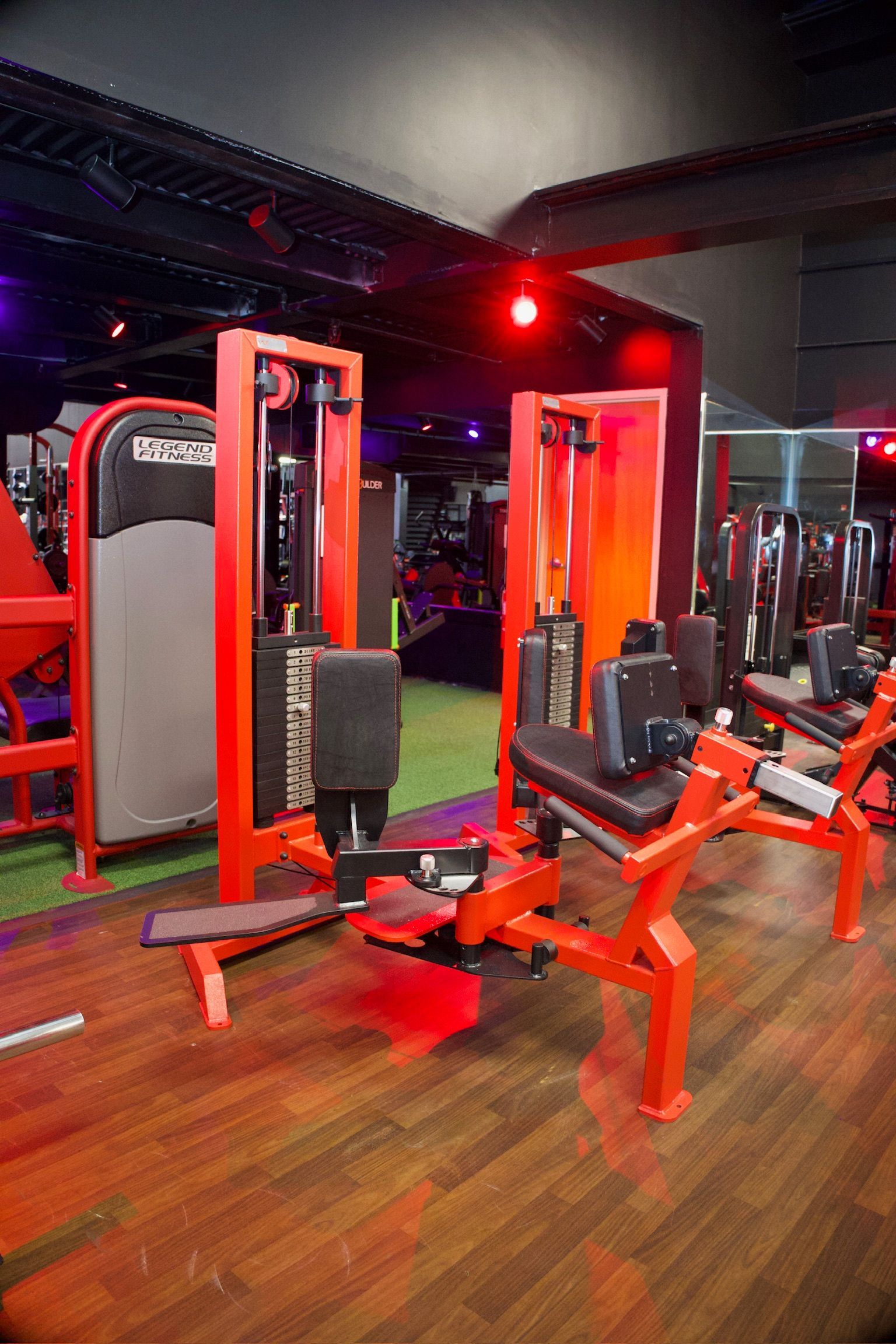Red weight machines in a gym with wood floors and a black ceiling.