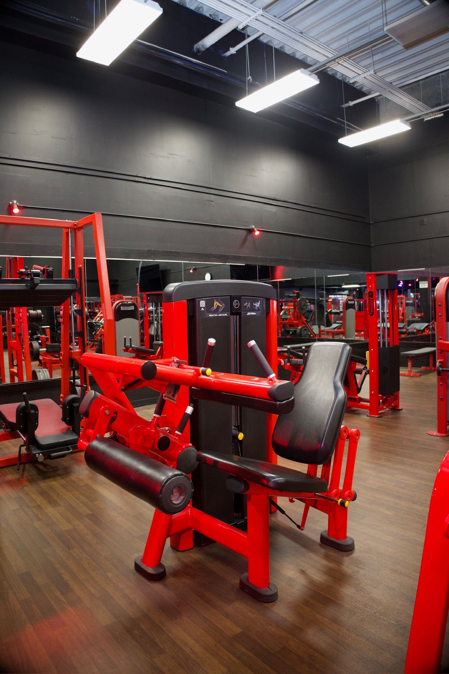 Red weight machines in a gym with dark walls and mirrored accents.
